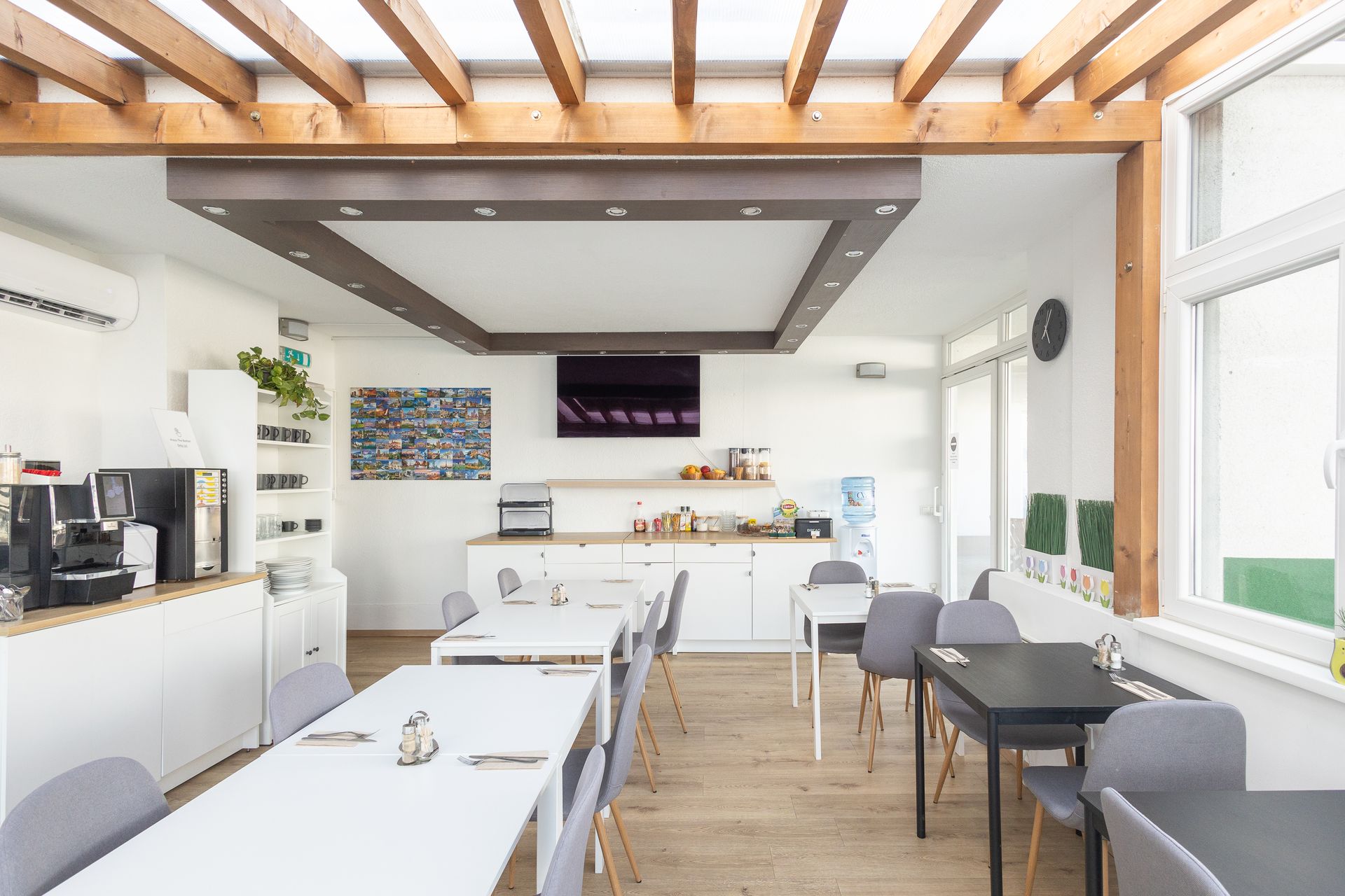 Breakfast room with tables and chairs under a wood-beamed ceiling. White cabinets, coffee maker, and TV.