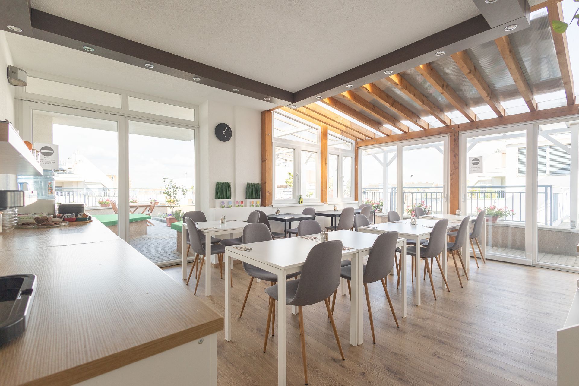 Bright dining area with tables, chairs, and large windows.  Wooden beams, light wood floors.