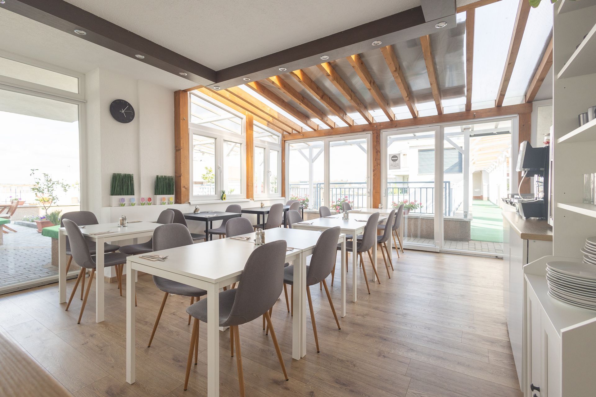 Bright dining area with white tables, gray chairs, and large windows.