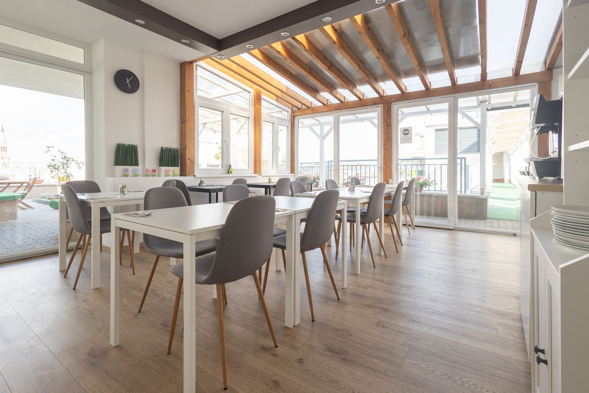 Bright, open room with long white tables, gray chairs, and large windows.