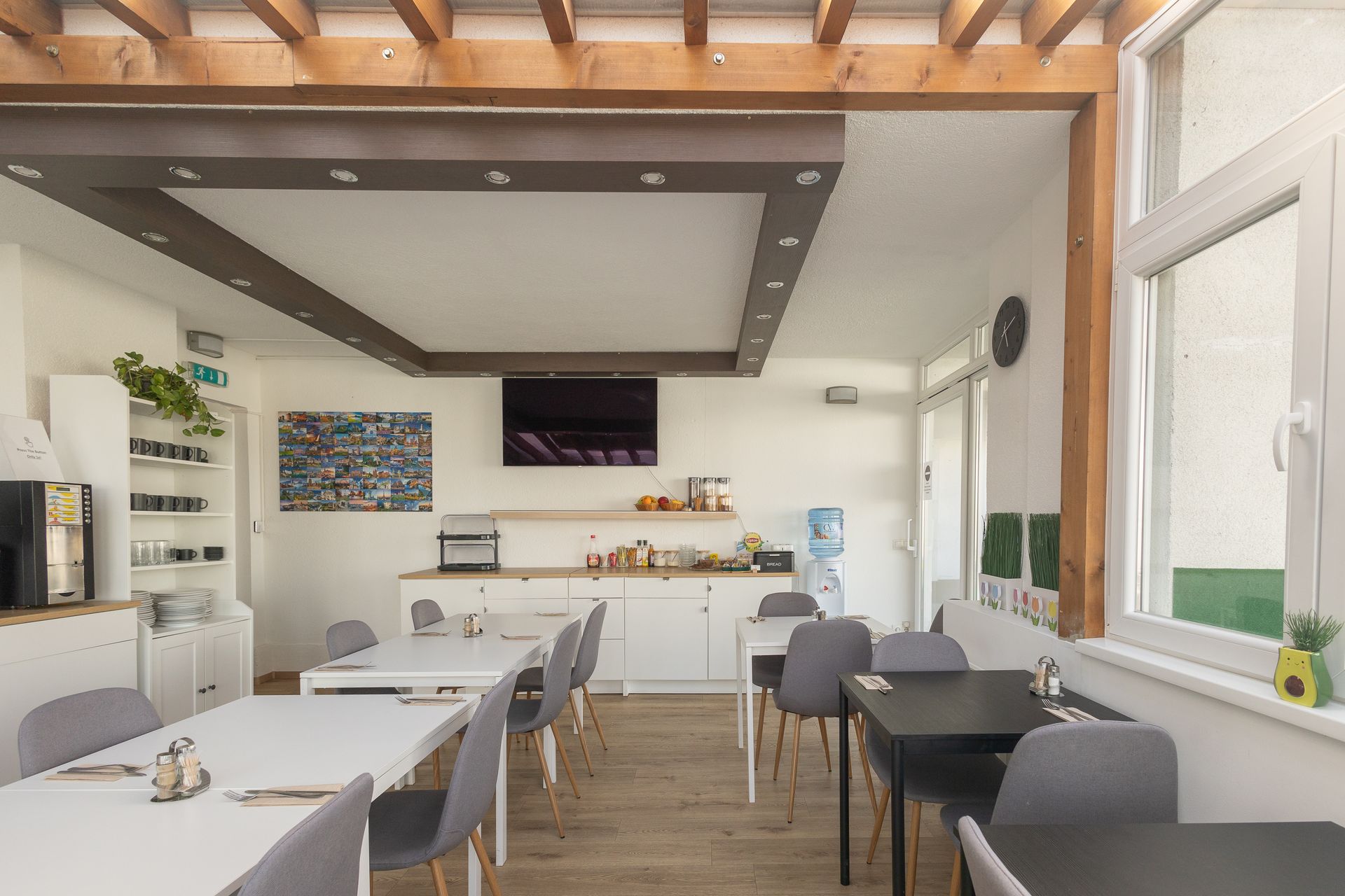 Dining area with tables and chairs. White walls and counters with a small TV and food preparation area.