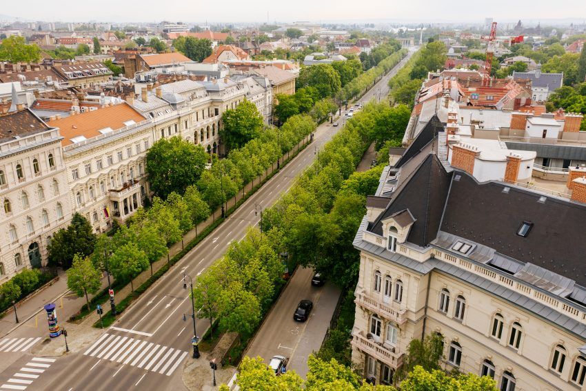 Aerial view of a wide boulevard lined with trees and buildings in a European city, sunny day.