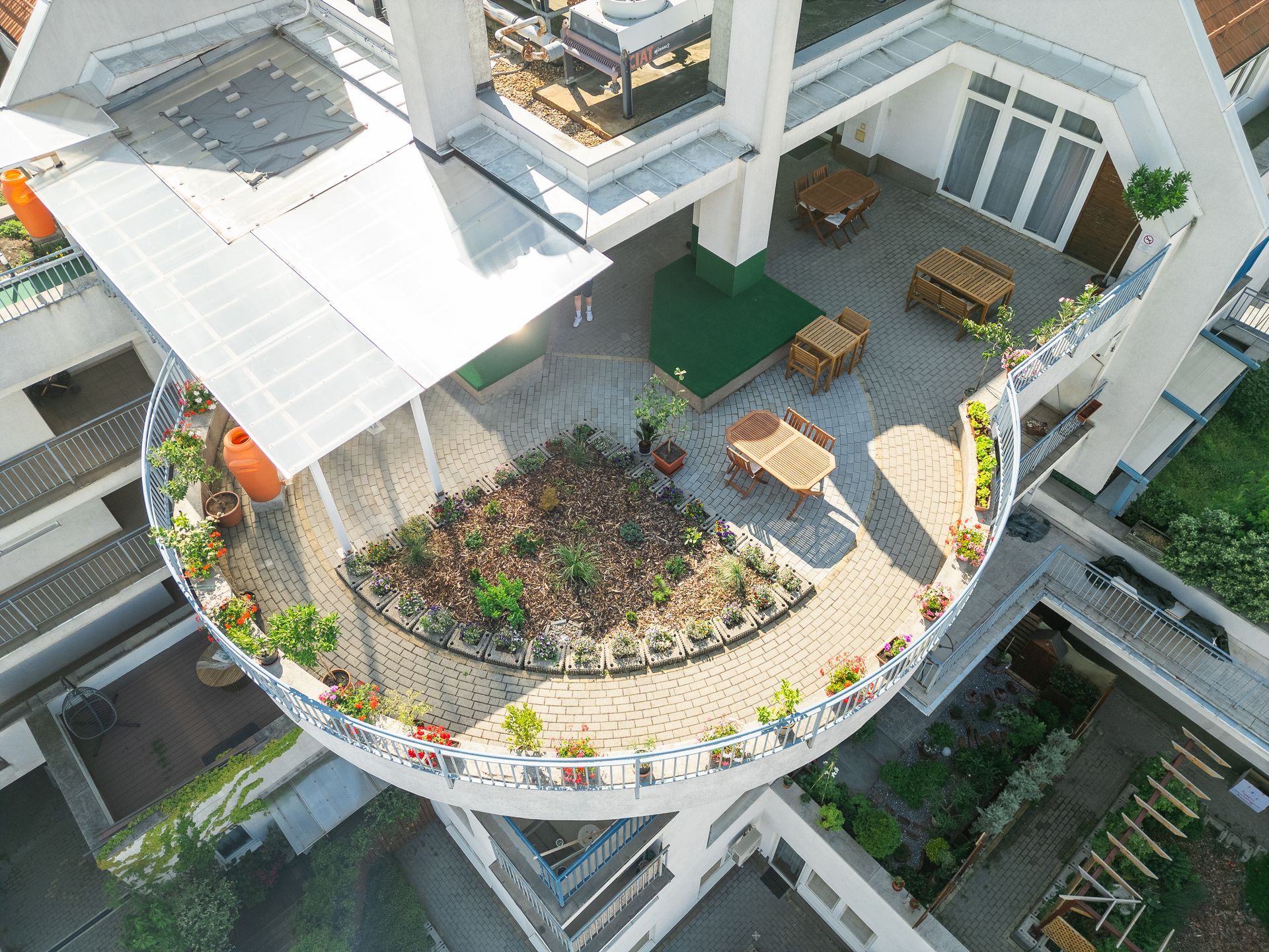 Aerial view of a rooftop garden with plants, tables, and a shaded area.