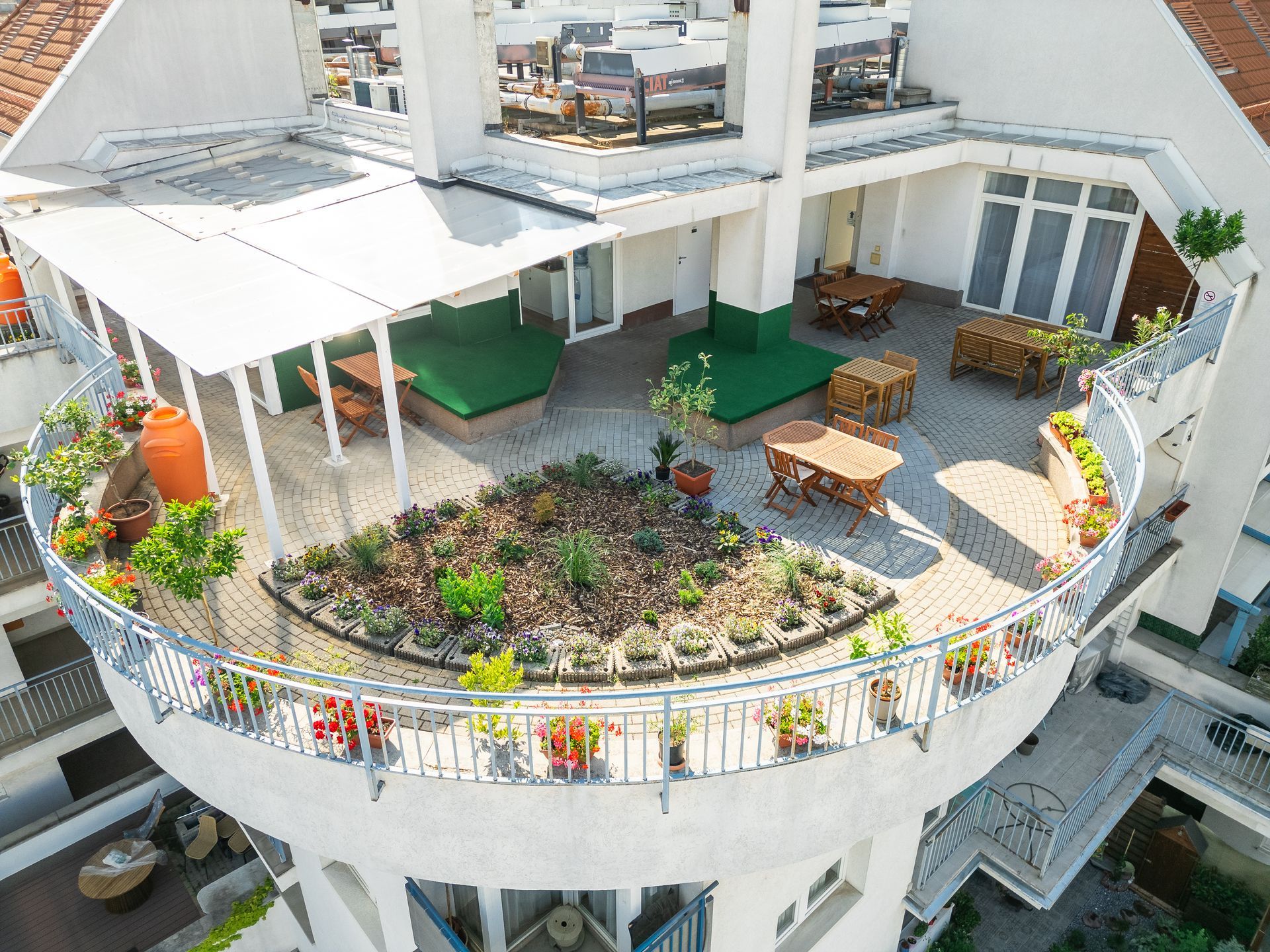 Rooftop terrace with green plants, seating, and a central garden bed surrounded by a metal railing.