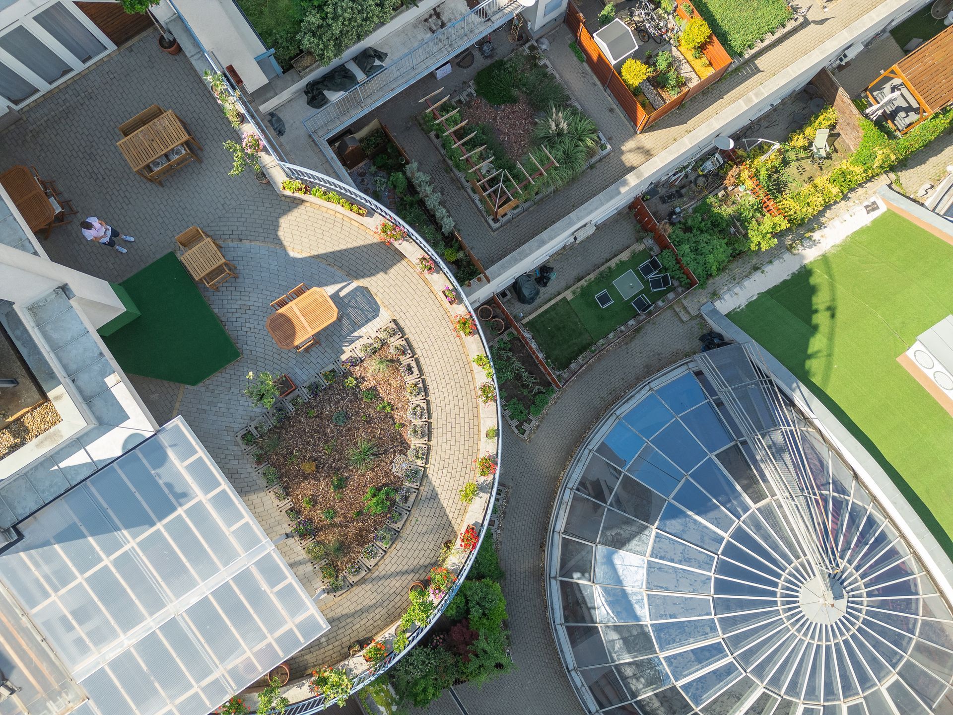 Aerial view of a rooftop garden with paths, benches, a greenhouse, and solar panels.