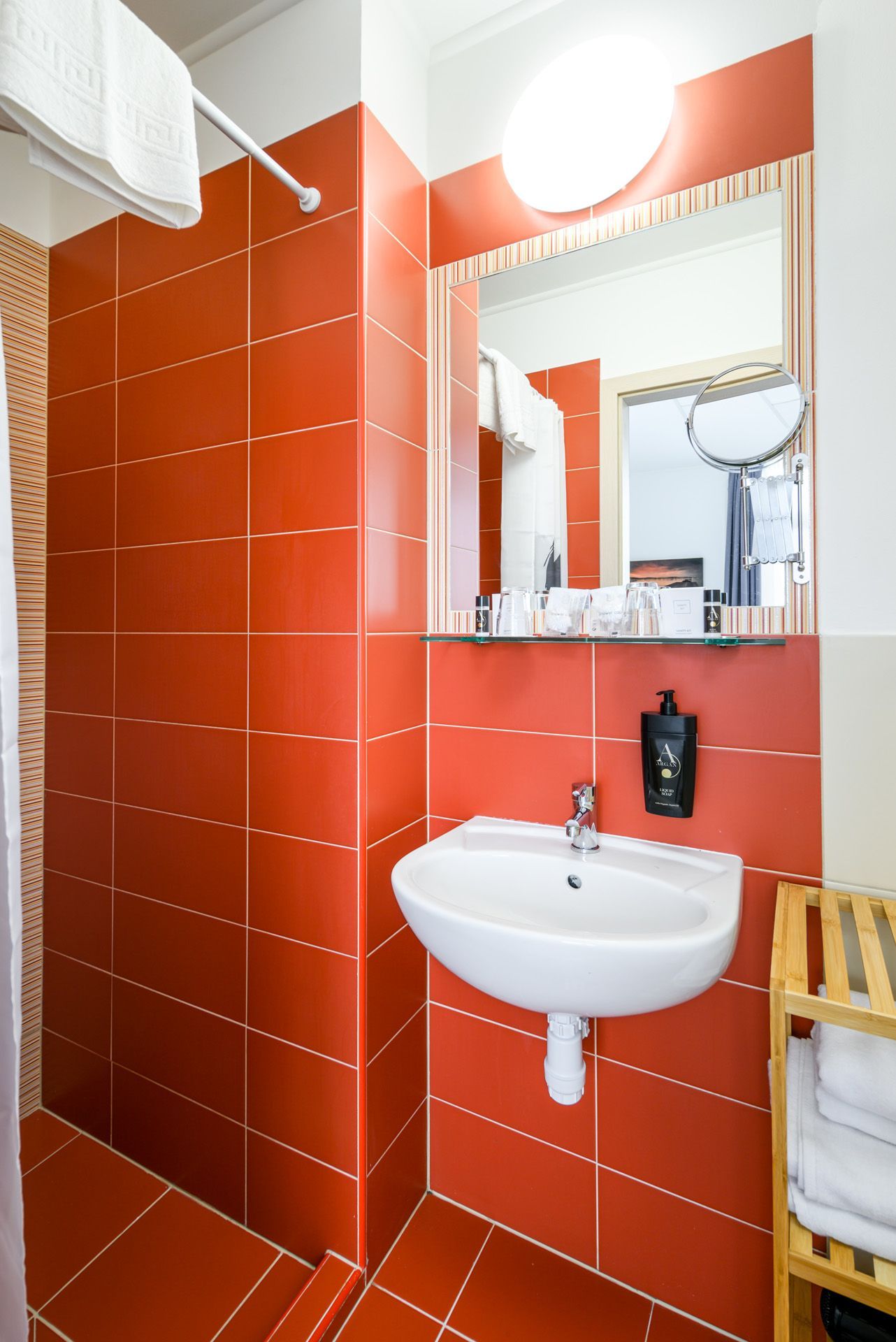Small bathroom with orange tiled walls, white sink, mirror, and toiletries.