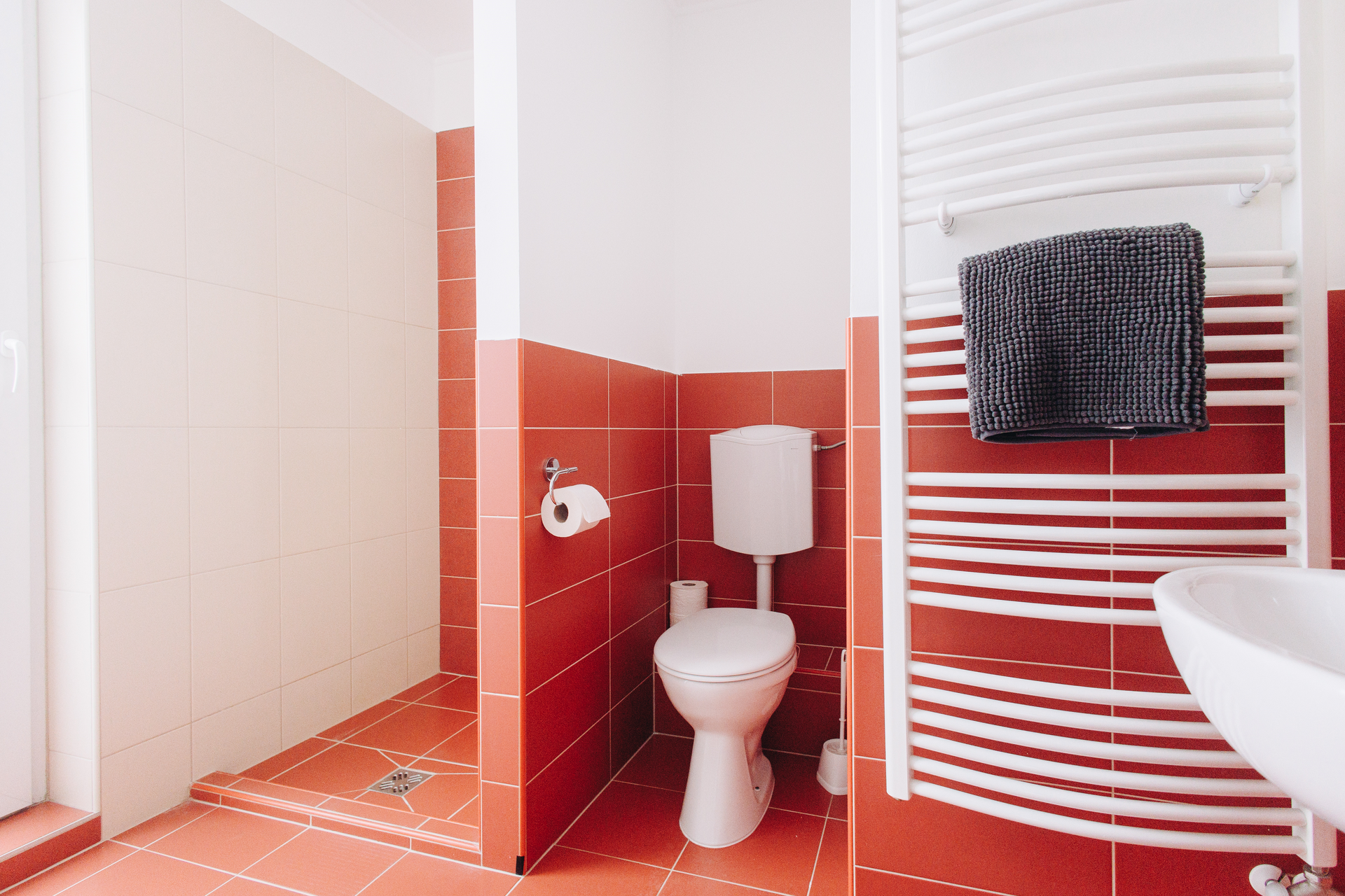 Bathroom with red tile, white toilet, and towel on a heated towel rack.