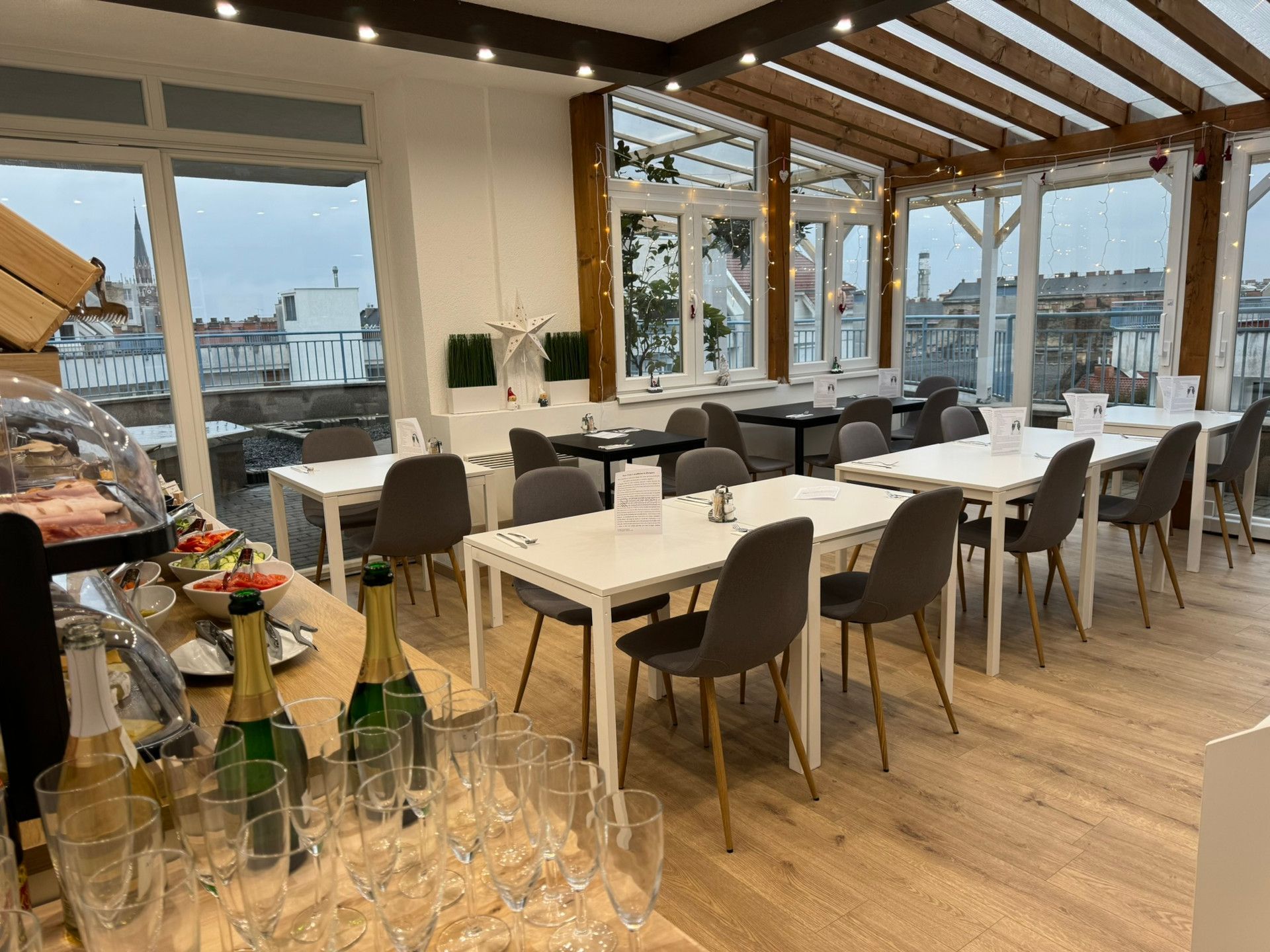 Bright dining room with white tables, gray chairs, and large windows overlooking a city.