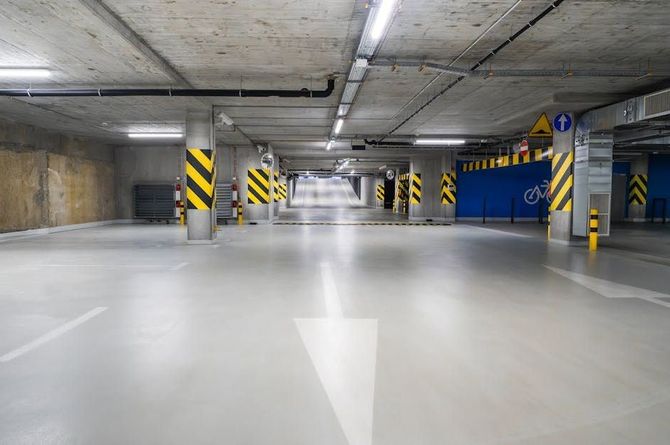 Empty underground parking garage with arrow marking direction, support pillars with yellow and black stripes.