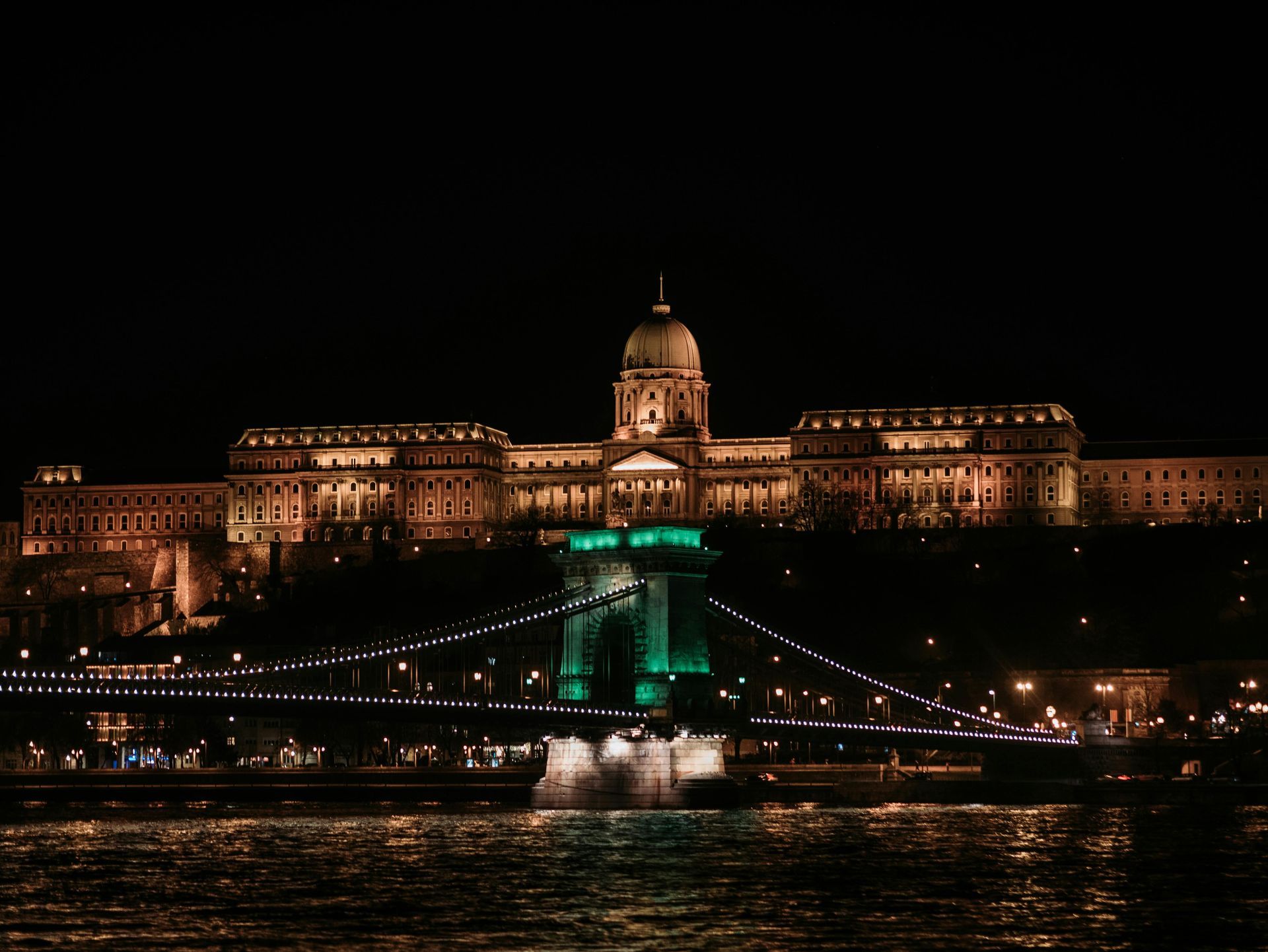 Budapest skyline at night with illuminated palace and bridge over the Danube River.