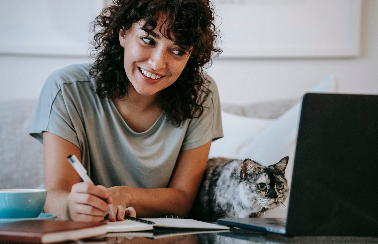 A woman sitting at a table with a laptop and a cat