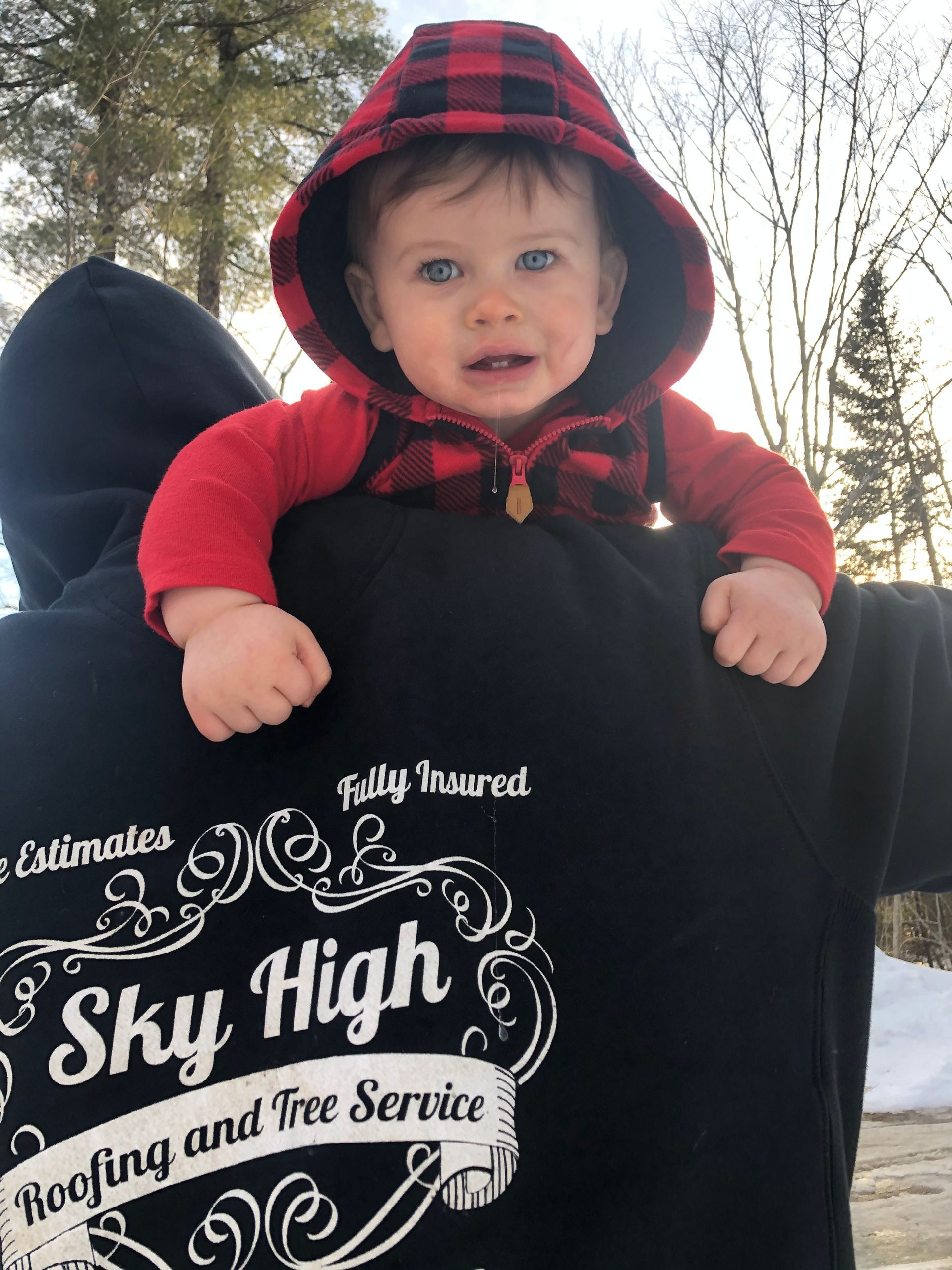 Baby in red plaid hoodie sits on a person wearing a black 