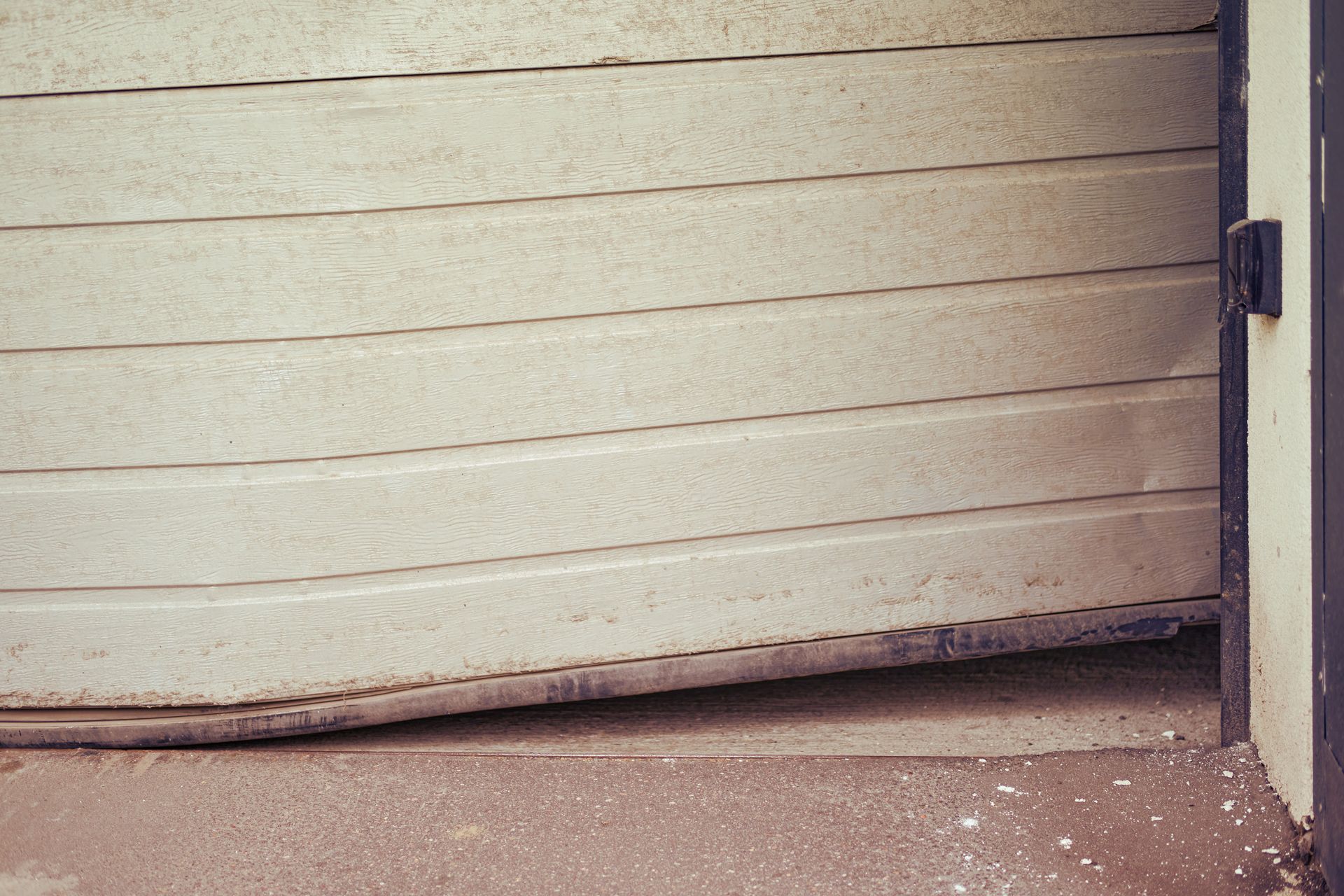 Partially opened, damaged garage door, white horizontal panels.