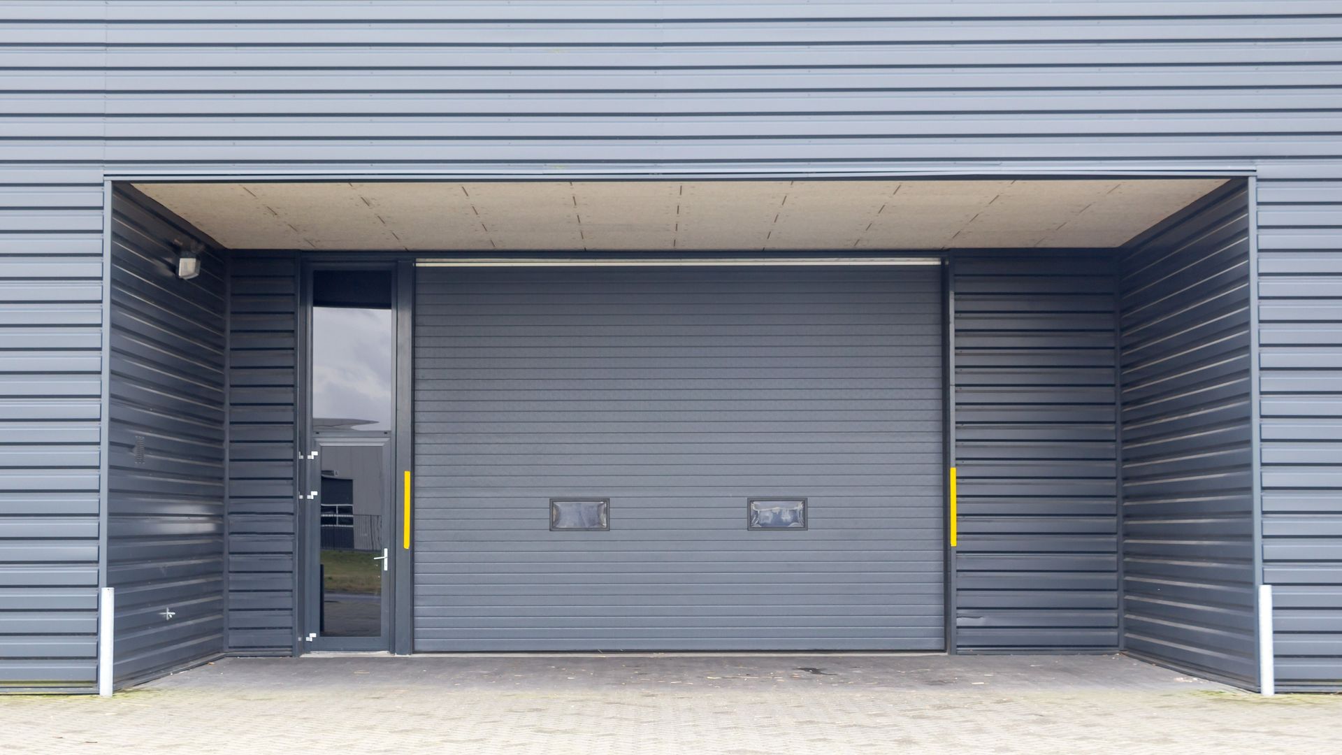 Gray industrial garage door in building facade with glass door to the left.