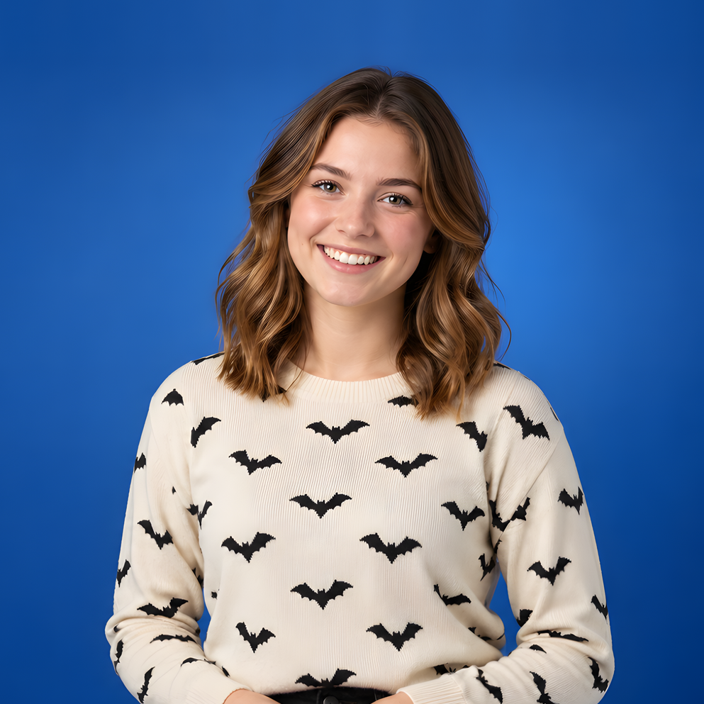 Smiling person in a cream sweater with black bat pattern against a blue background