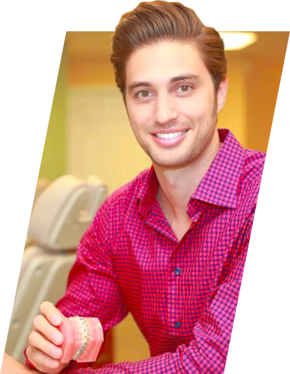 A man in a pink shirt is smiling and holding a model of his teeth.