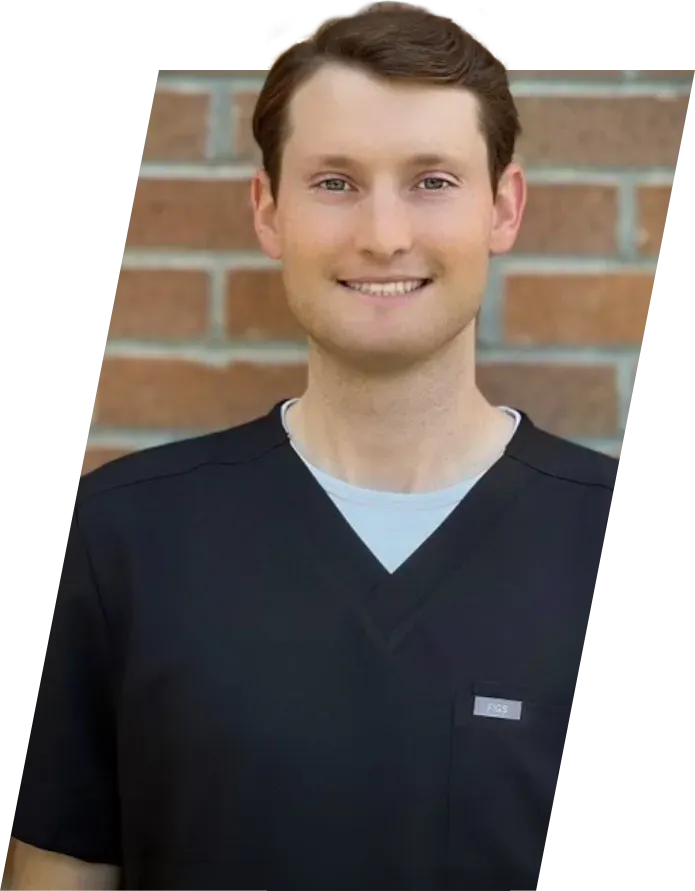 Smiling person in black scrubs leans against a brick wall.