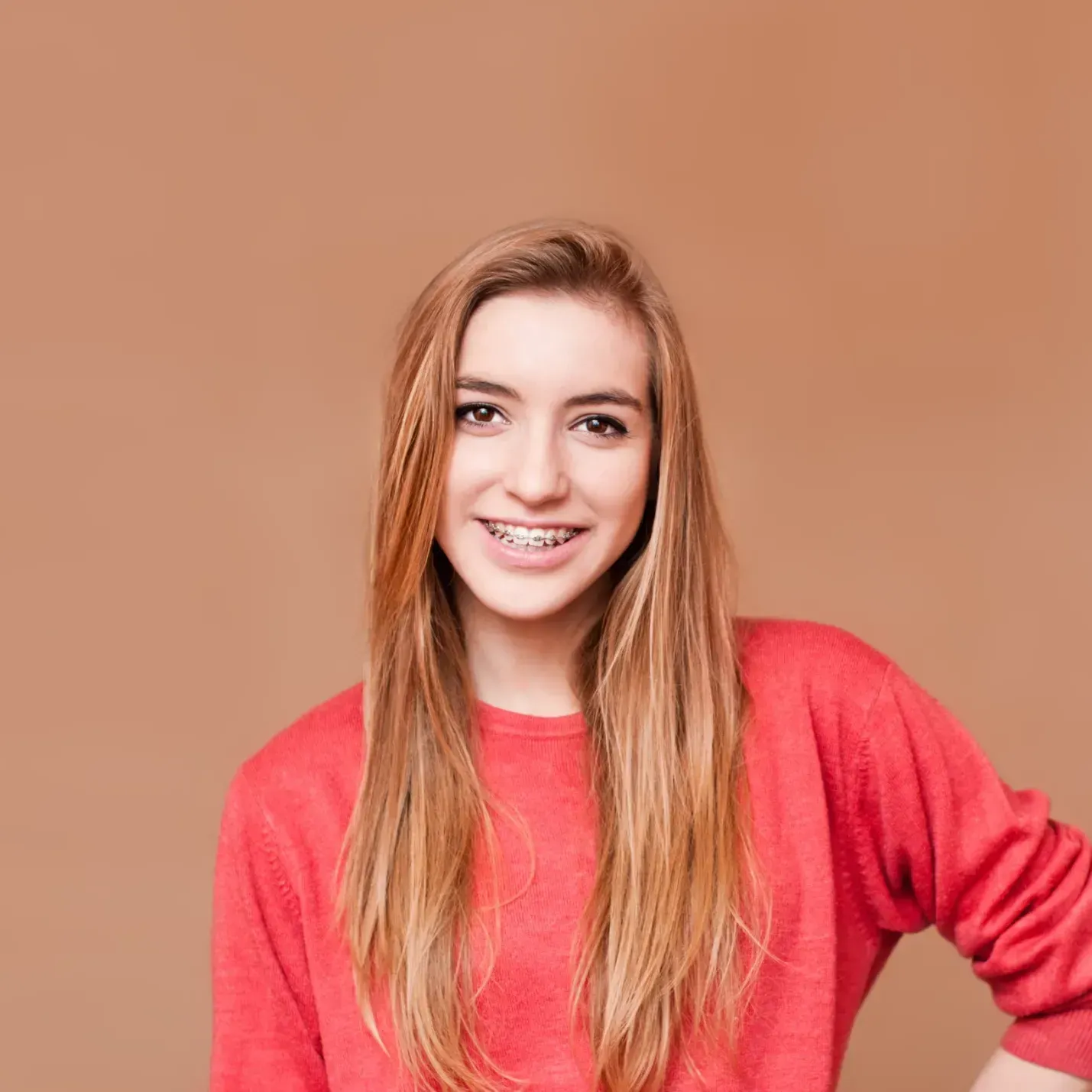 A young woman with braces on her teeth is wearing a red sweater and smiling.
