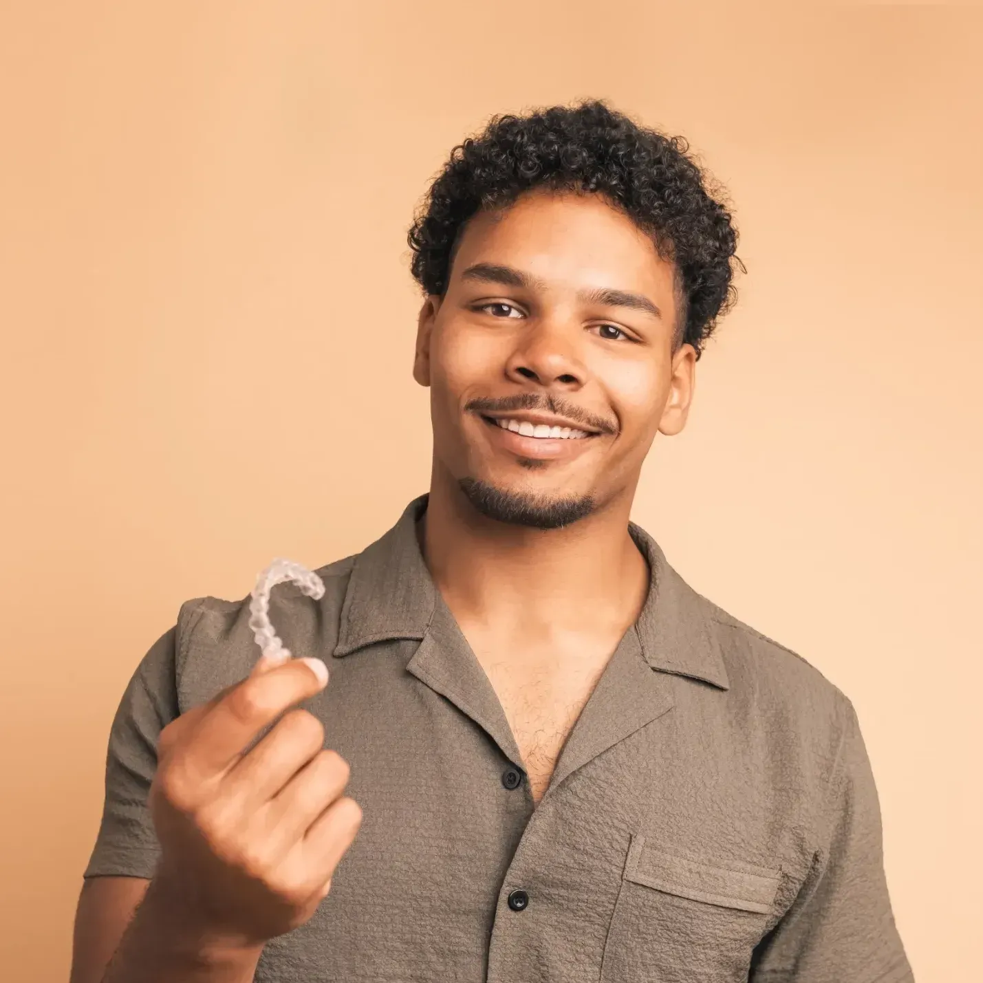 A man in a grey shirt is holding a clear brace in his hand.