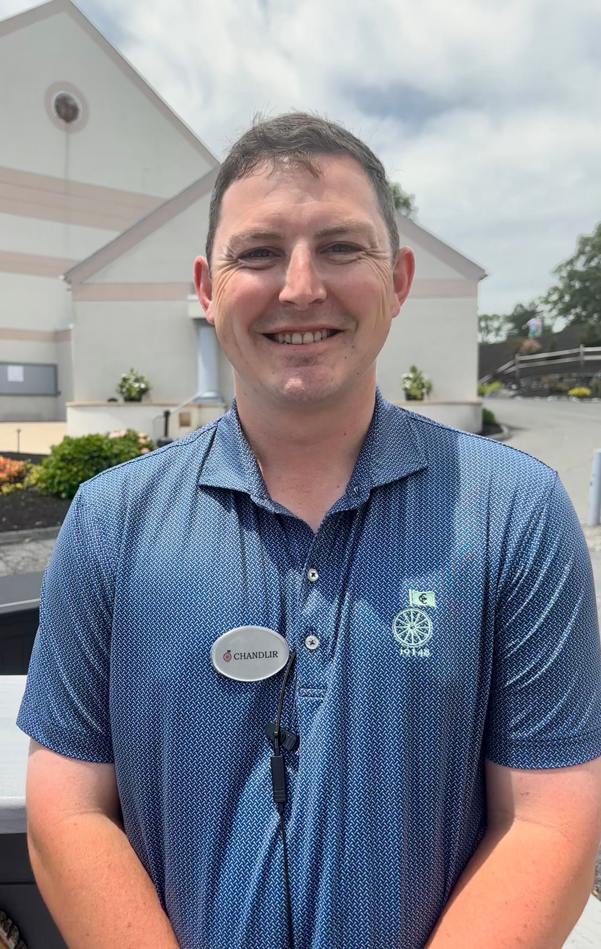 Smiling man in blue patterned polo standing outside a building