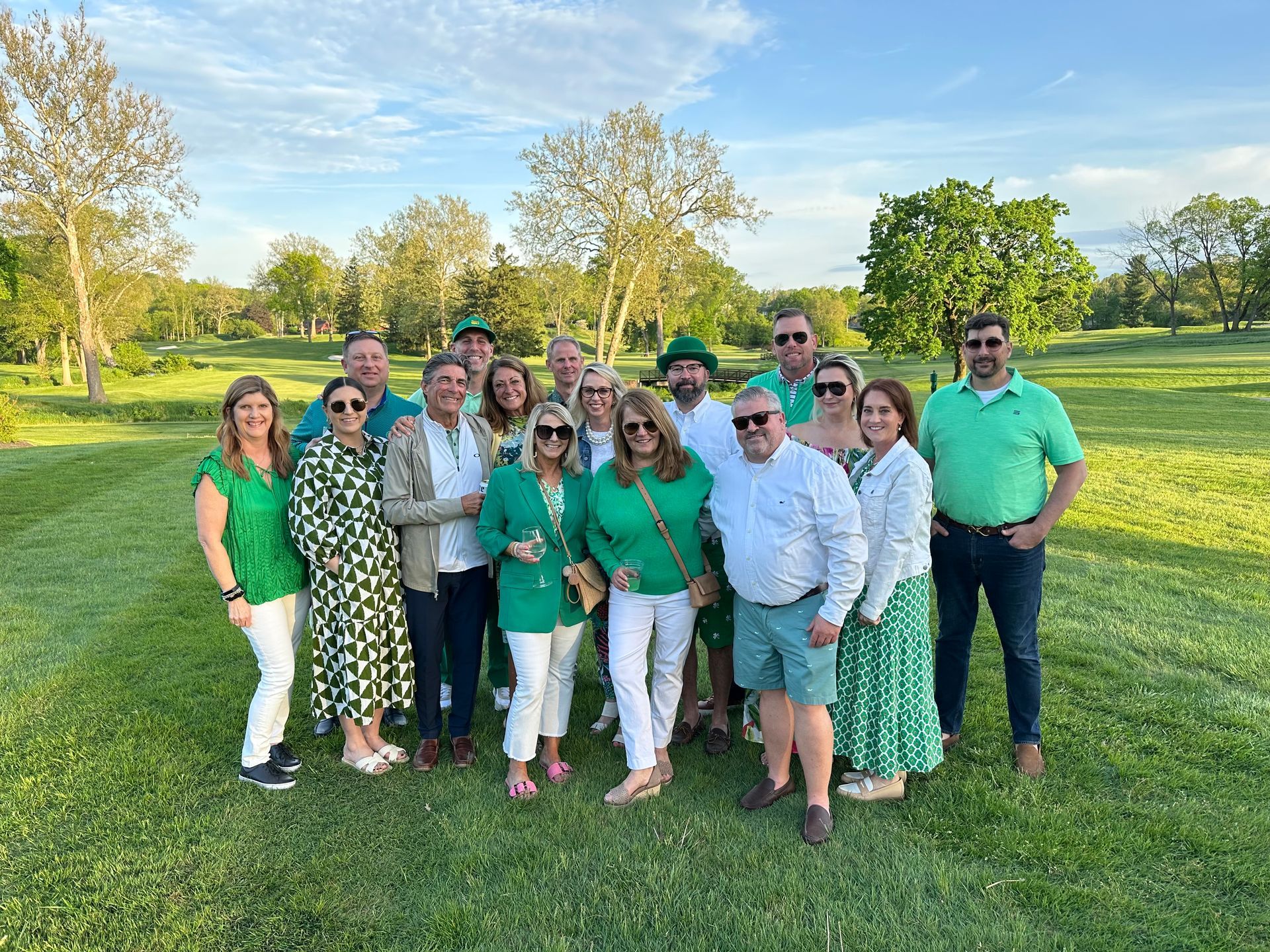 Group of people in green and white outfits posing together on a sunny golf course