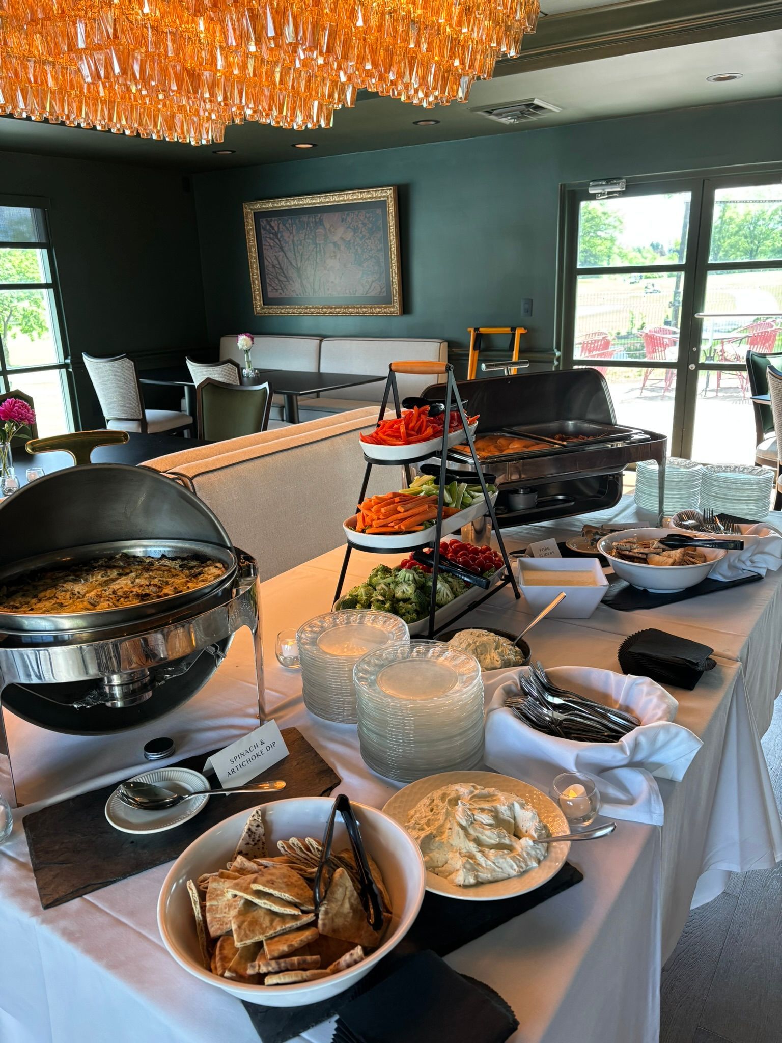 Buffet table with breakfast foods and serving dishes in a bright dining room near large windows