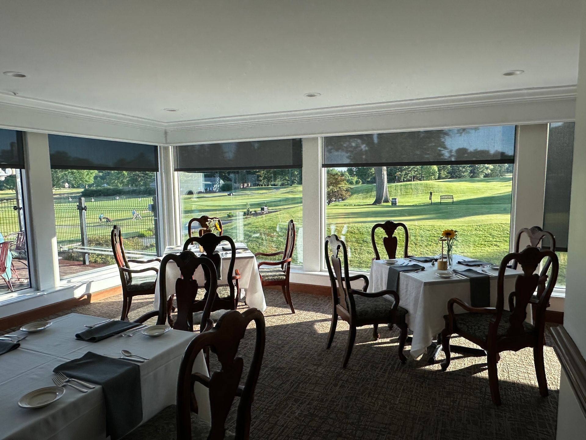 Bright dining room with tables and chairs overlooking a green lawn through large windows.
