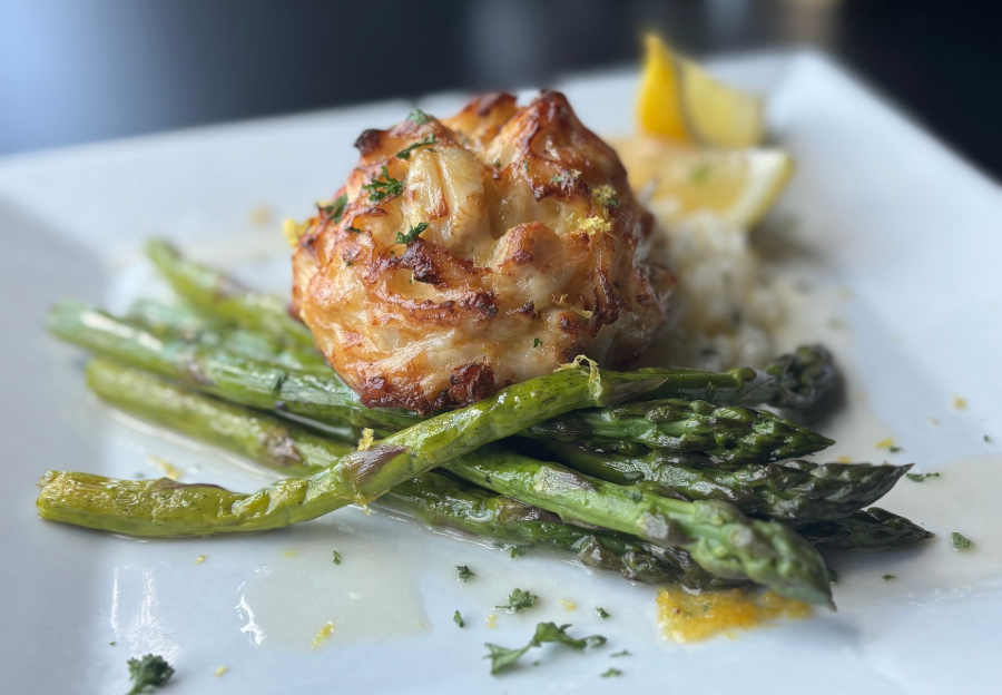 Grilled asparagus and a browned crab cake on a white plate with lemon wedges