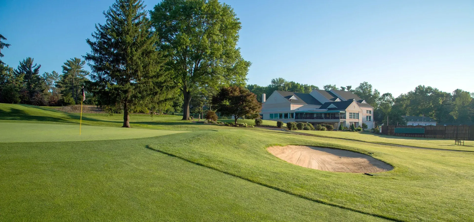Golf course green with a sand bunker, trees, and houses in the background