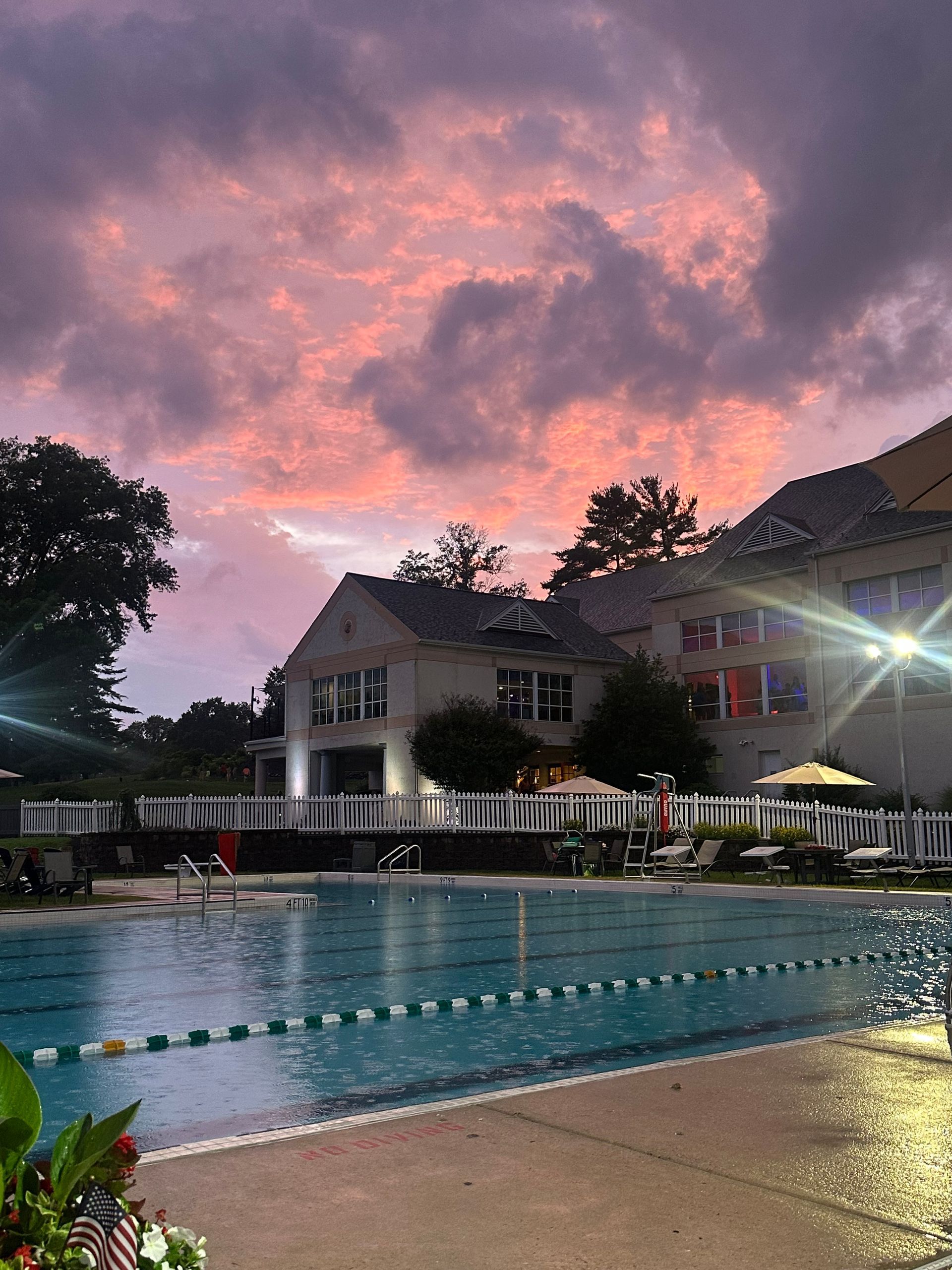 Outdoor pool at dusk with pink clouds, a lit building, and calm water reflections