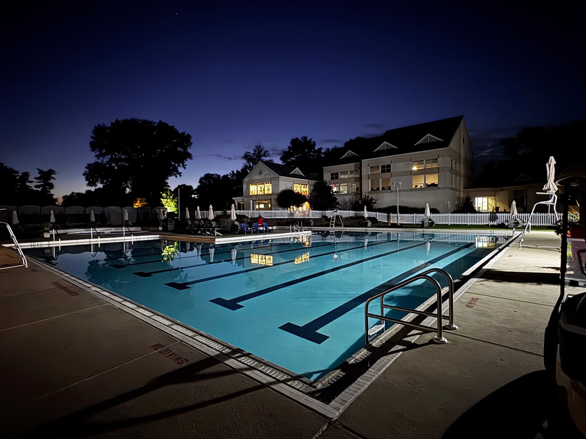 Nighttime outdoor swimming pool with bright lights and building reflections nearby