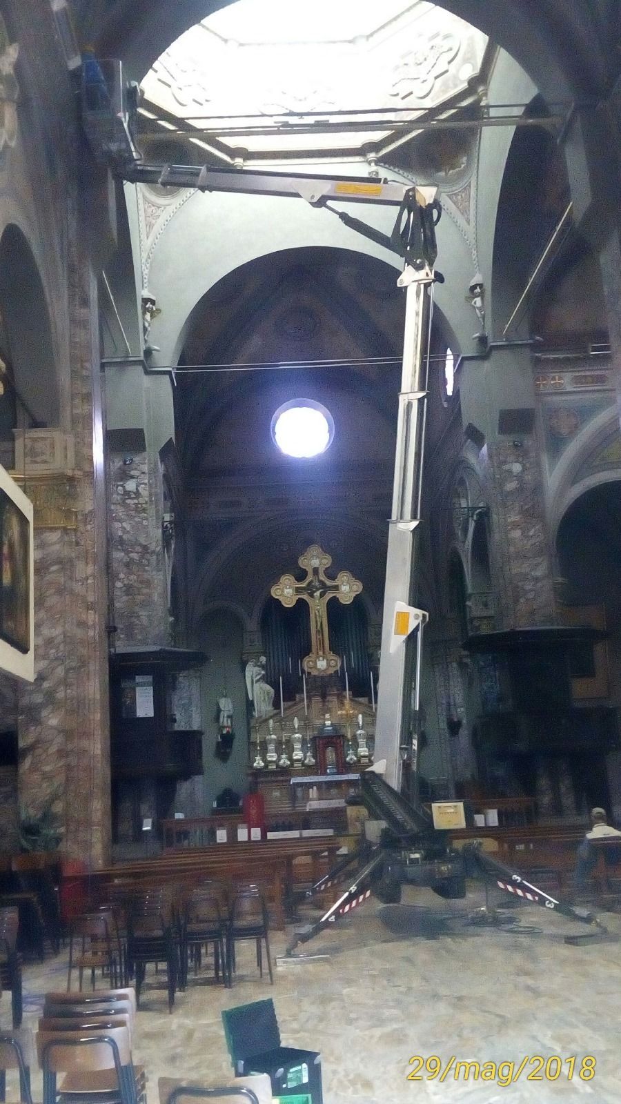 Interno della chiesa con piattaforma elevatrice sollevata verso il soffitto. Croce e altare visibili.