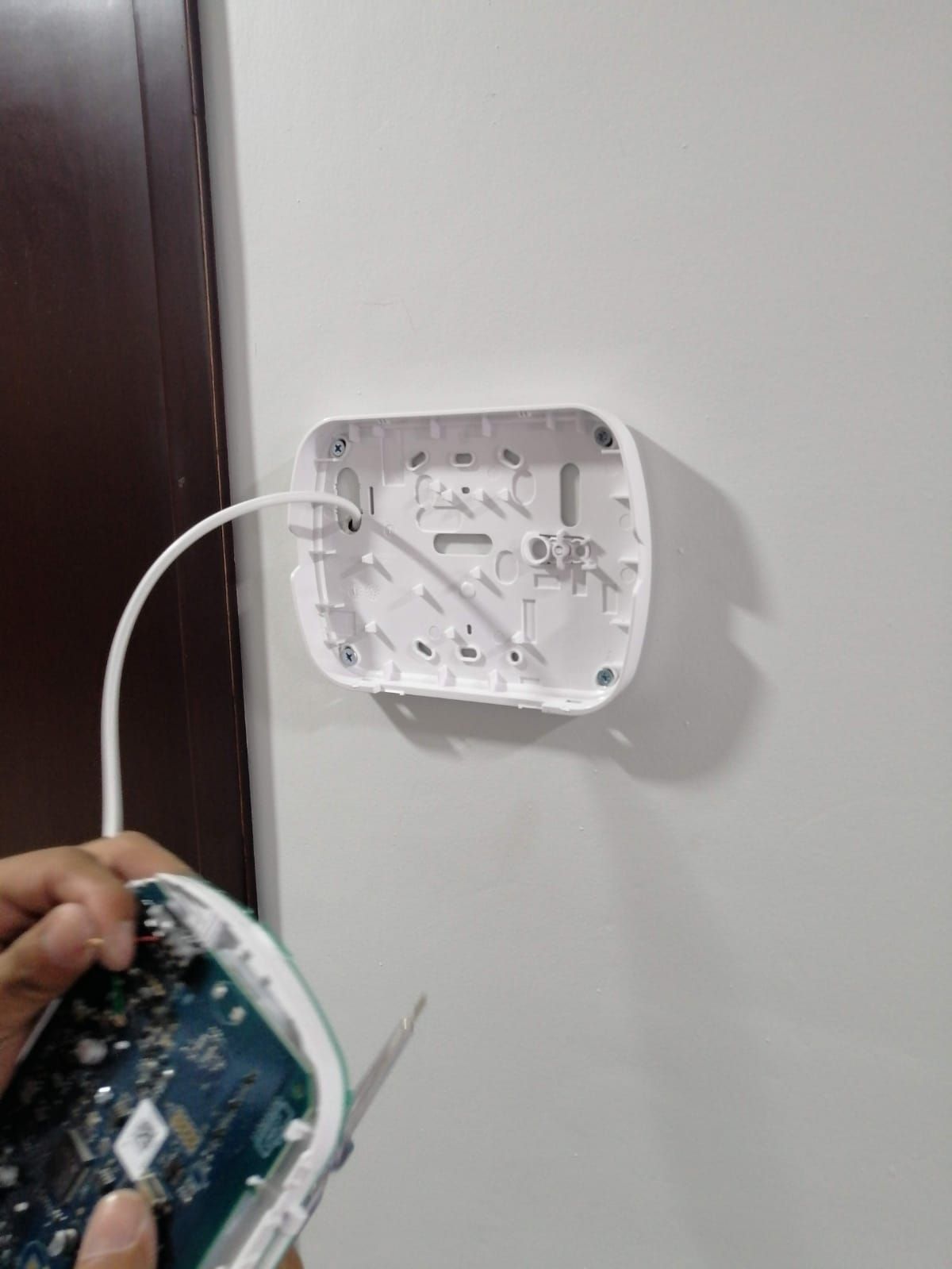 Una persona está montando un dispositivo blanco en una pared blanca, mostrando el cableado interno.