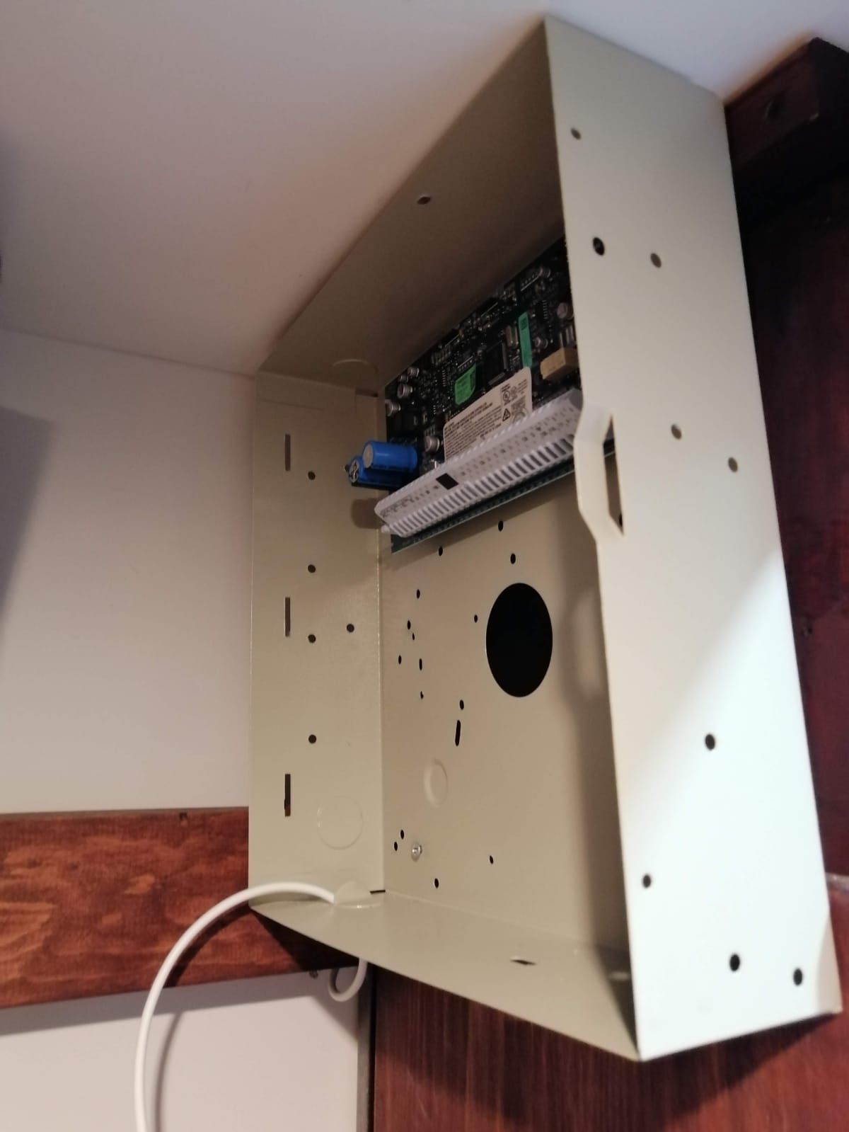 Panel de control del sistema de seguridad abierto montado en una pared; cable blanco extensible.