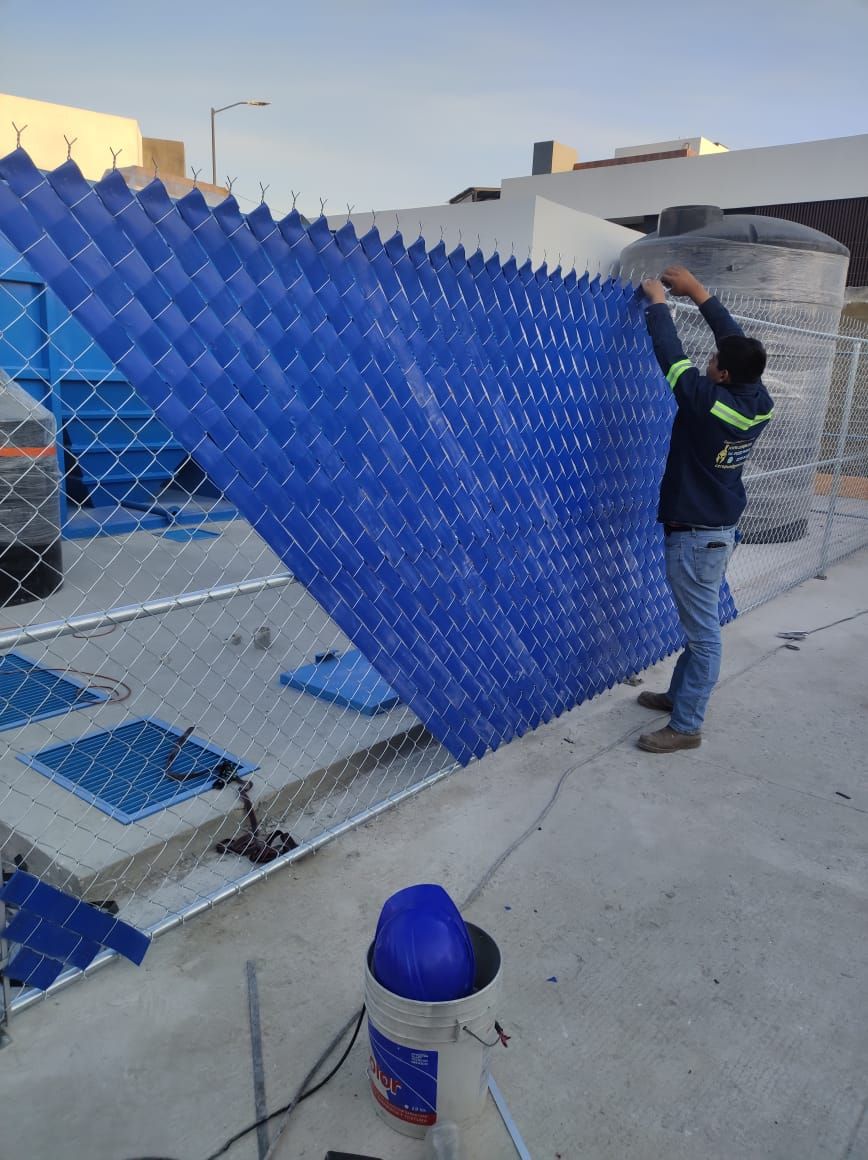 Hombre instalando paneles azules de relleno para una torre de refrigeración en un tejado. También se ven una valla y tanques de agua.