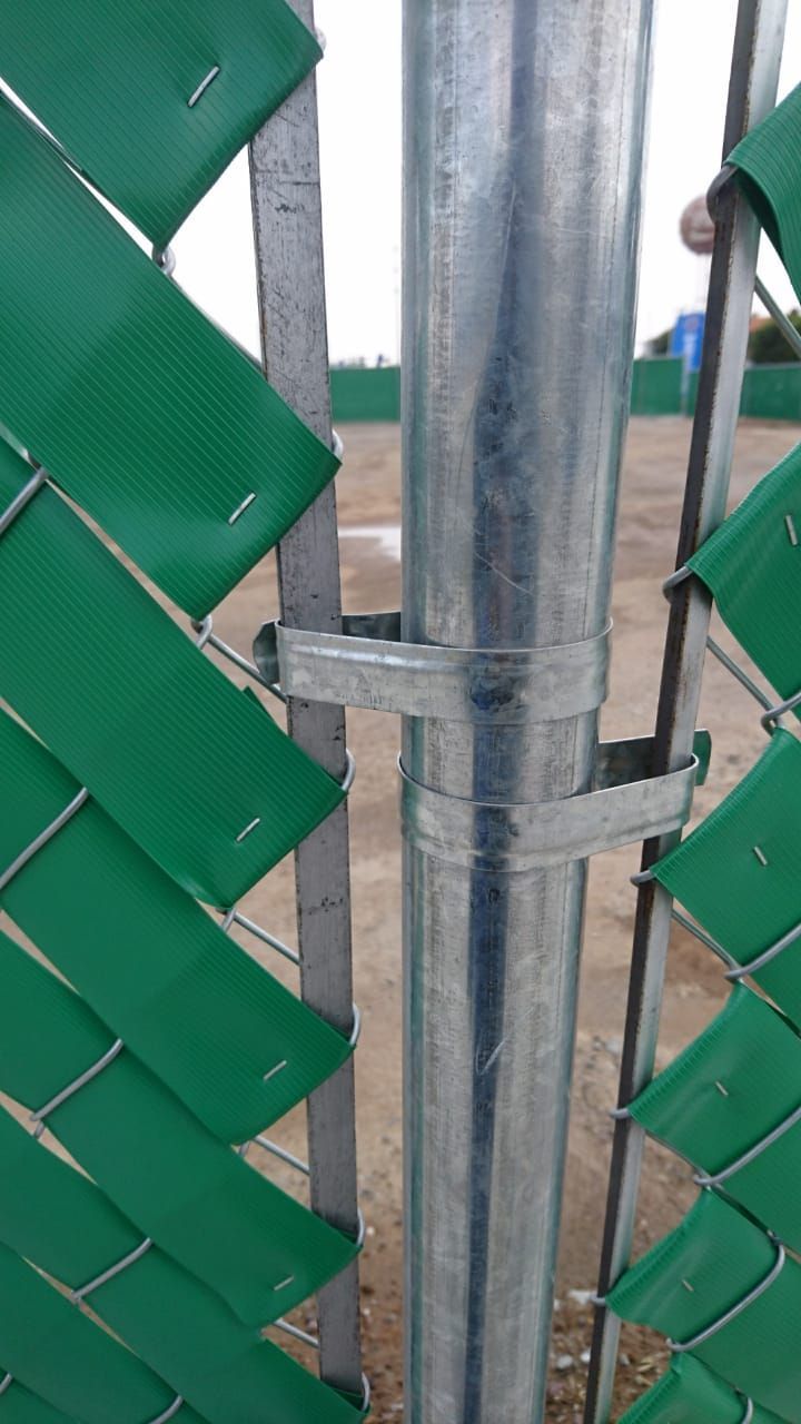 Valla de alambre verde con un poste de metal asegurado por dos soportes de metal.