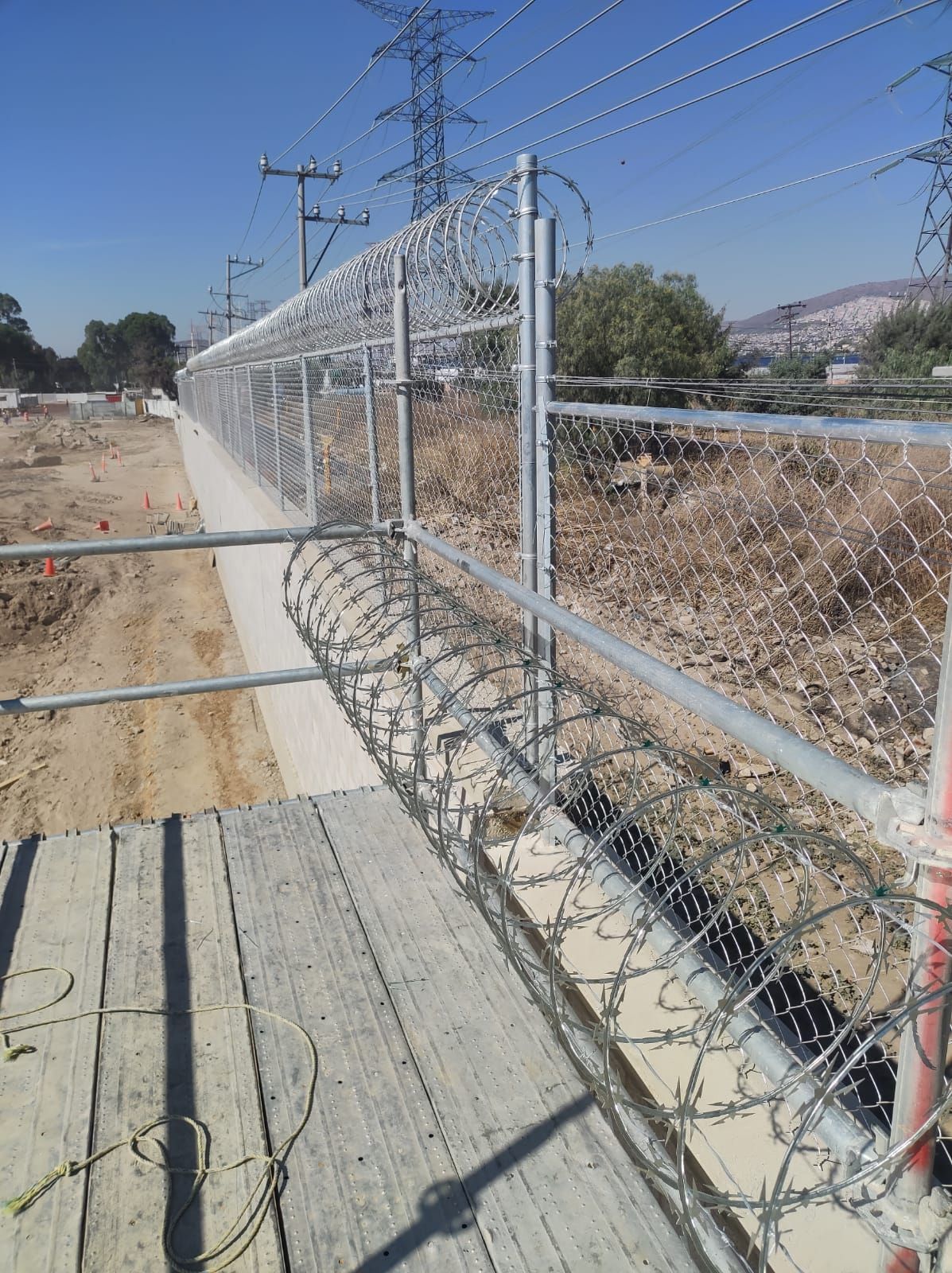 Valla de alambre de espino sobre una plataforma de hormigón. Cables eléctricos al fondo.