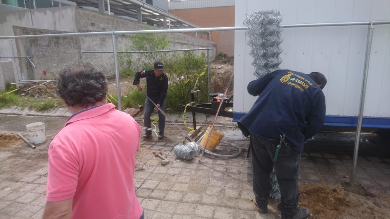 Tres hombres trabajan en la construcción cerca de un remolque blanco. Uno excava, otro trabaja con malla de alambre y el tercero observa.