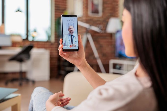 A woman is sitting on a couch holding a cell phone with a doctor on it.