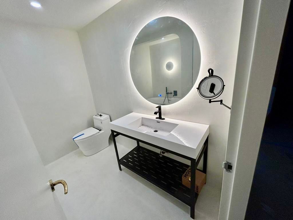 Bright modern bathroom with oval mirror, white vanity, and round wall light.