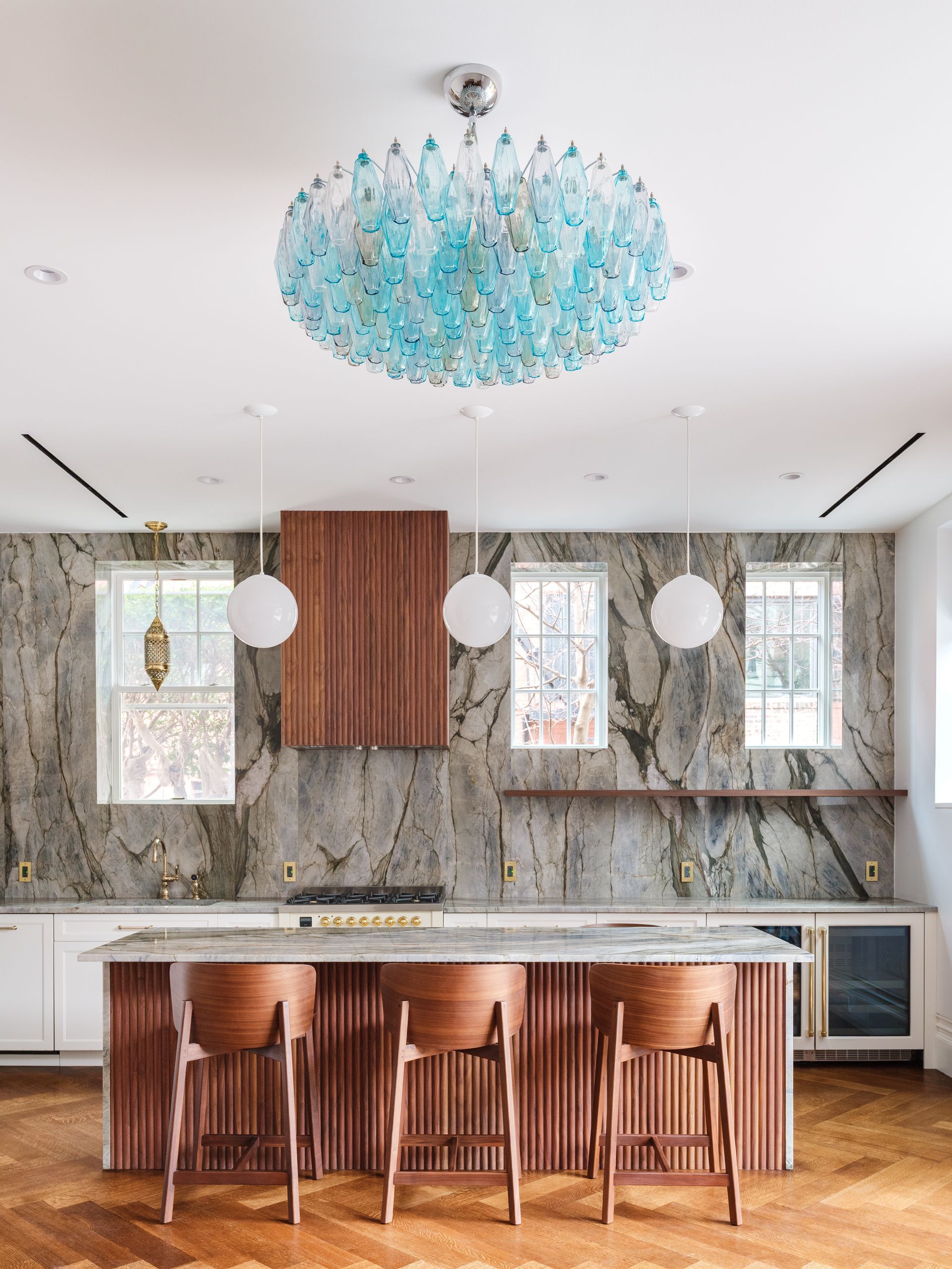 Modern kitchen with marble backsplash, wood island seating, and a blue chandelier