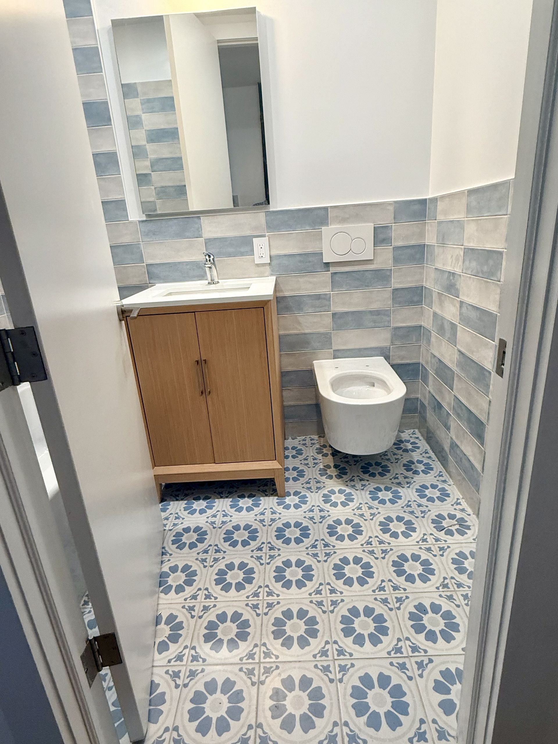 Small bathroom with blue patterned tile, wooden vanity, mirror cabinet, and wall-mounted toilet