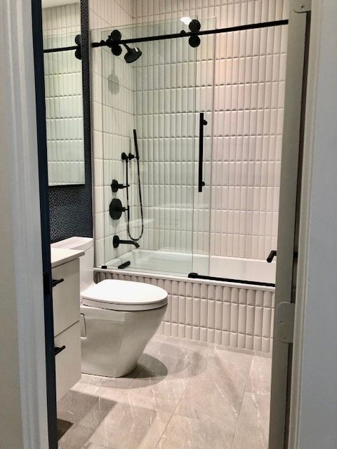 Modern bathroom with a walk-in shower, black fixtures, white tile, and a toilet in the foreground