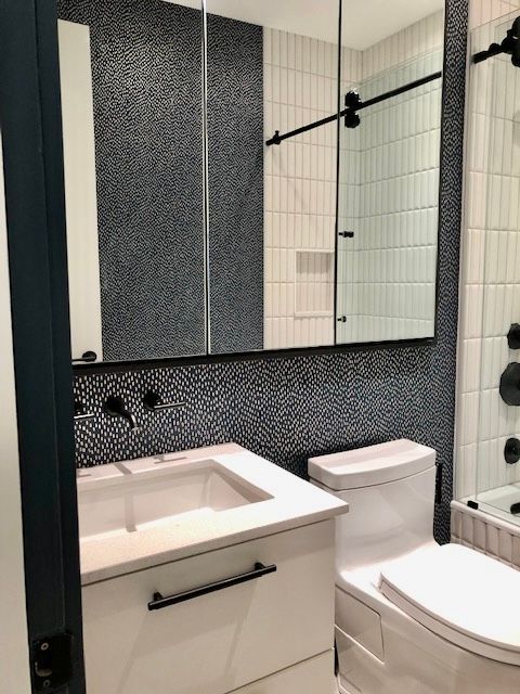Modern bathroom with white vanity, sink, toilet, and patterned black-and-white tile walls.