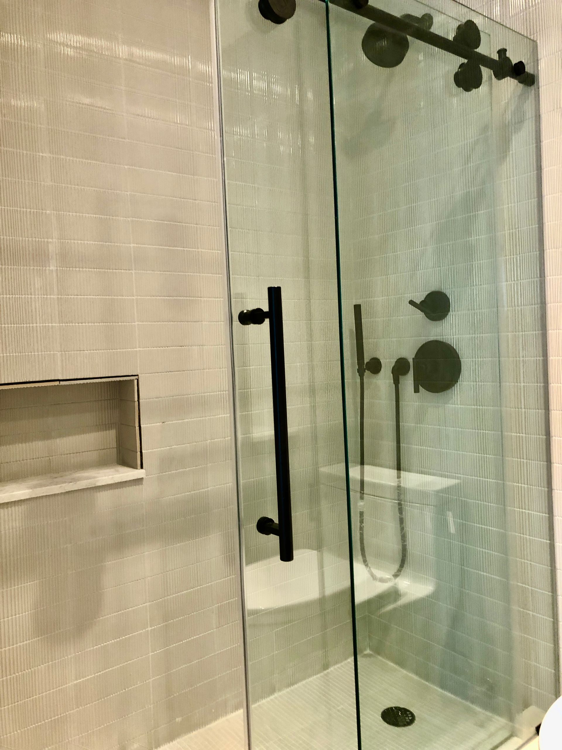 Glass shower enclosure with black hardware, beige tile walls, and a bench inside