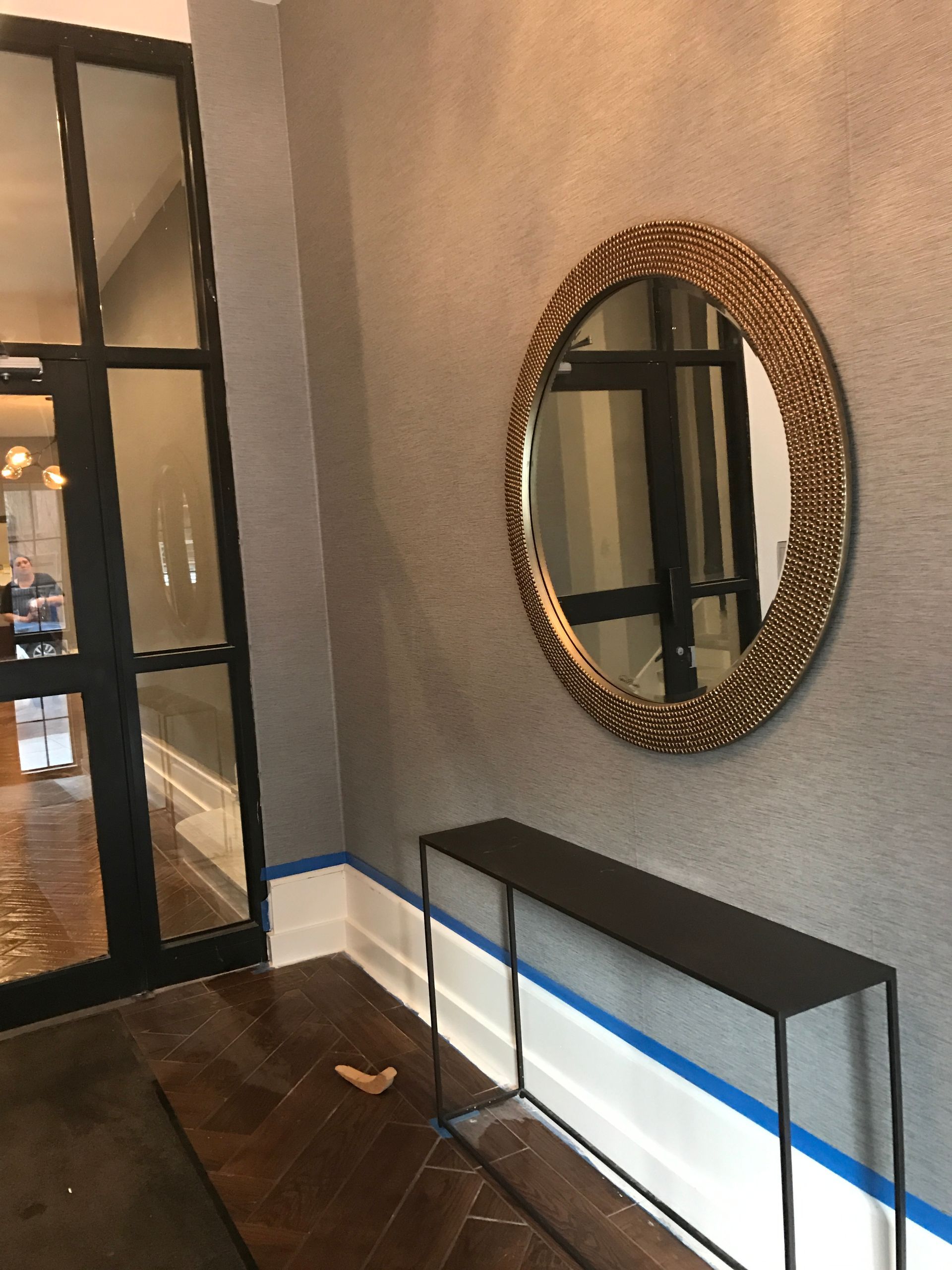 Hallway with a glass door, round mirror, and black-and-white console table against a textured wall.