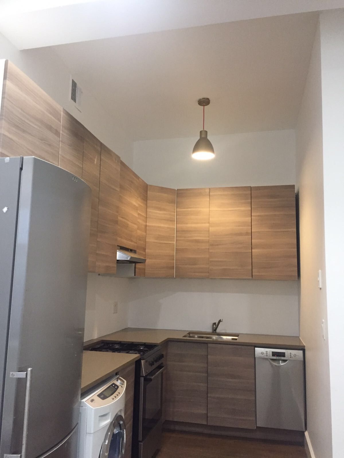 Small modern kitchen with wood cabinets, stainless fridge and dishwasher, and a hanging light.