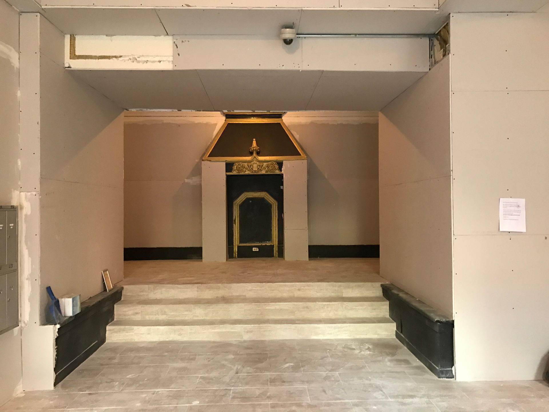 Steps leading to a small ornate gold-and-black altar in a plain interior alcove