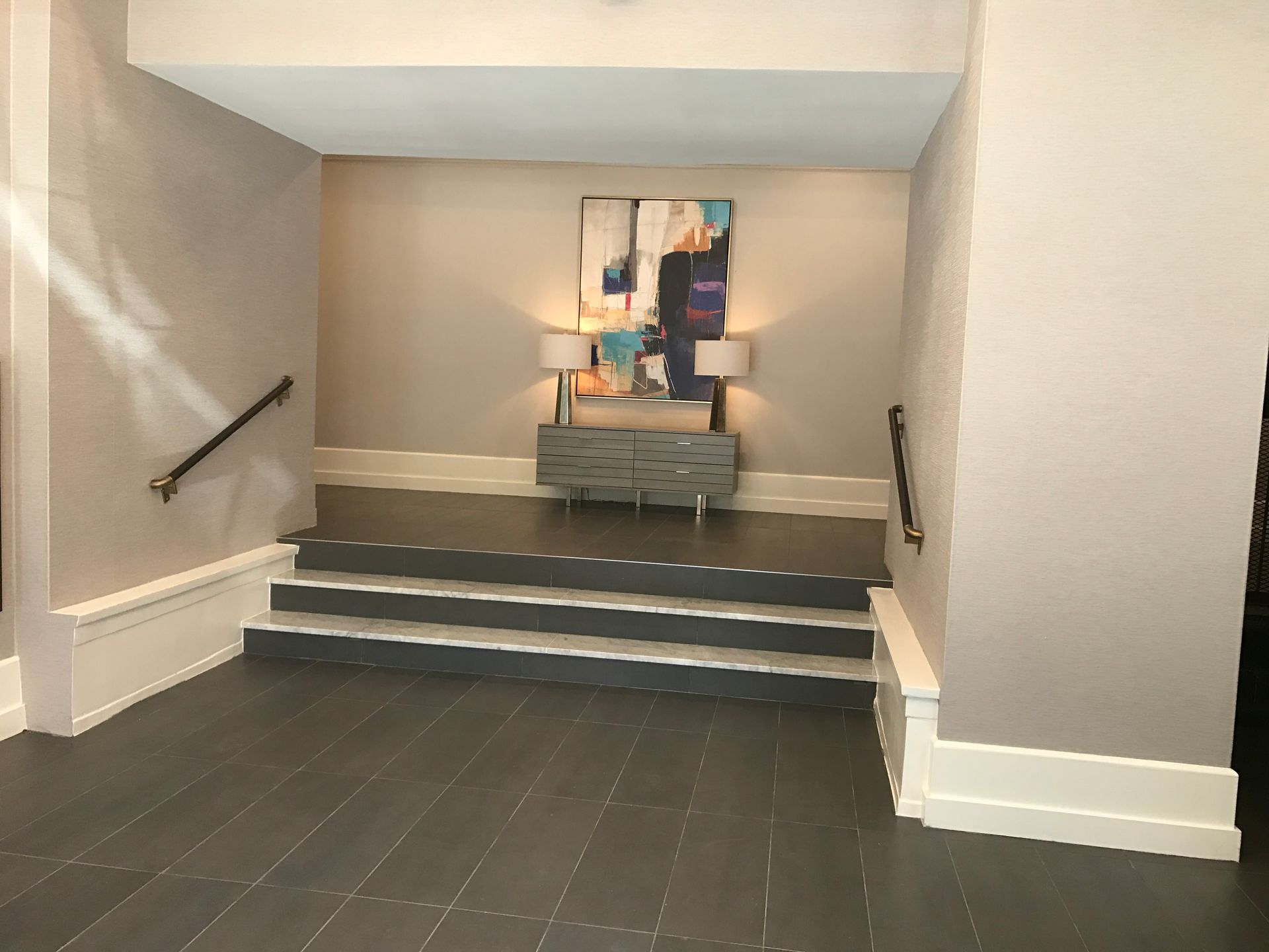 Empty stairwell landing with gray tile steps, wall handrails, and artwork at the top.