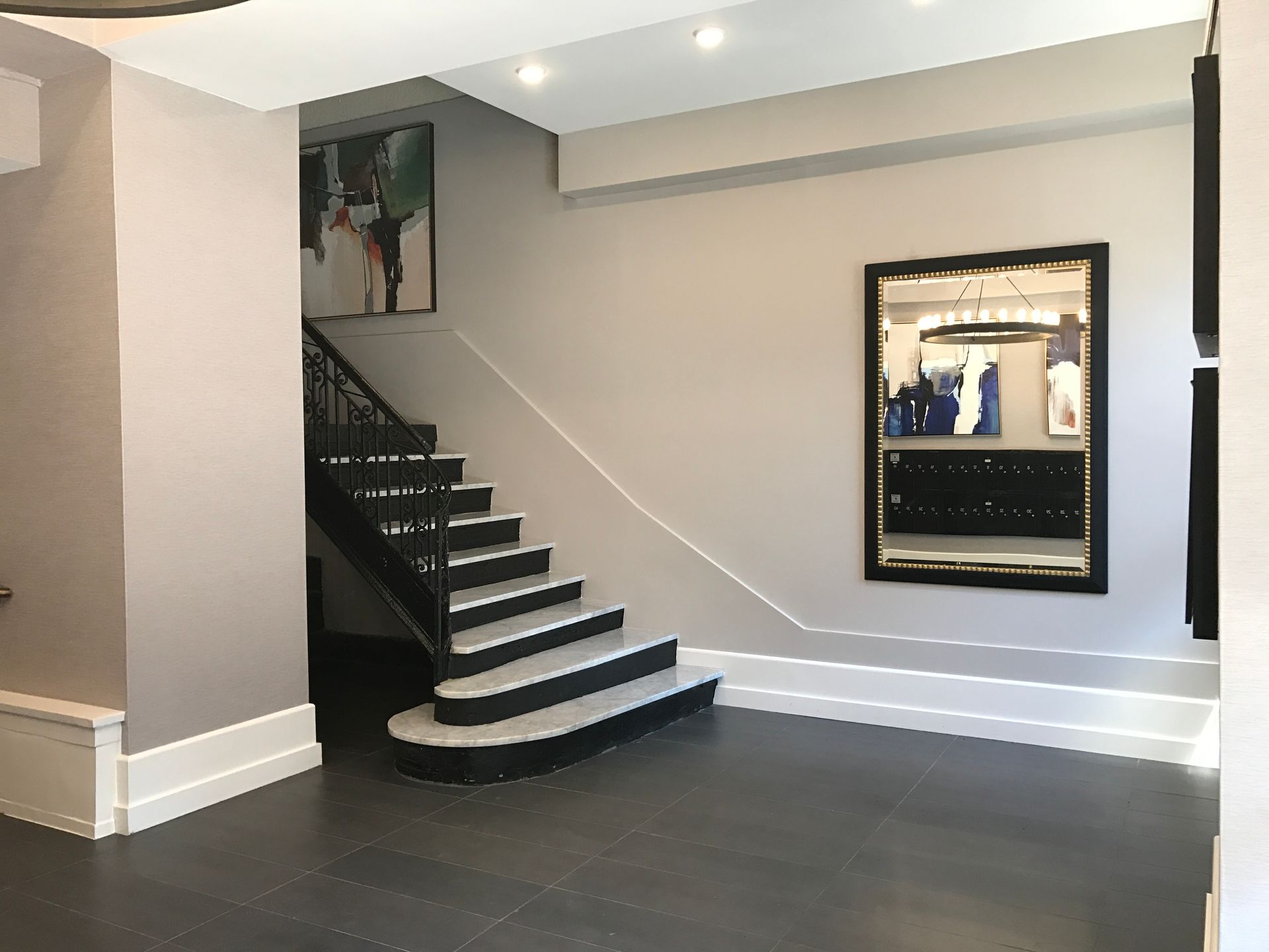 Interior staircase with black steps and white railing in a gray-walled hallway, with a framed mirror on the right.